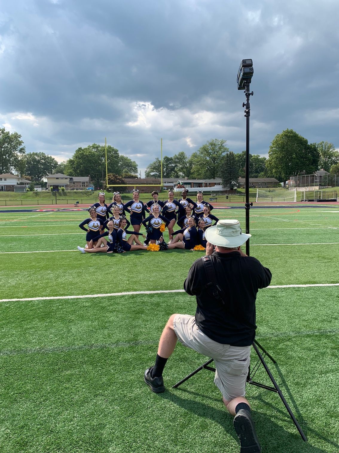 Photographer capturing a posed group on a sports field under a cloudy sky