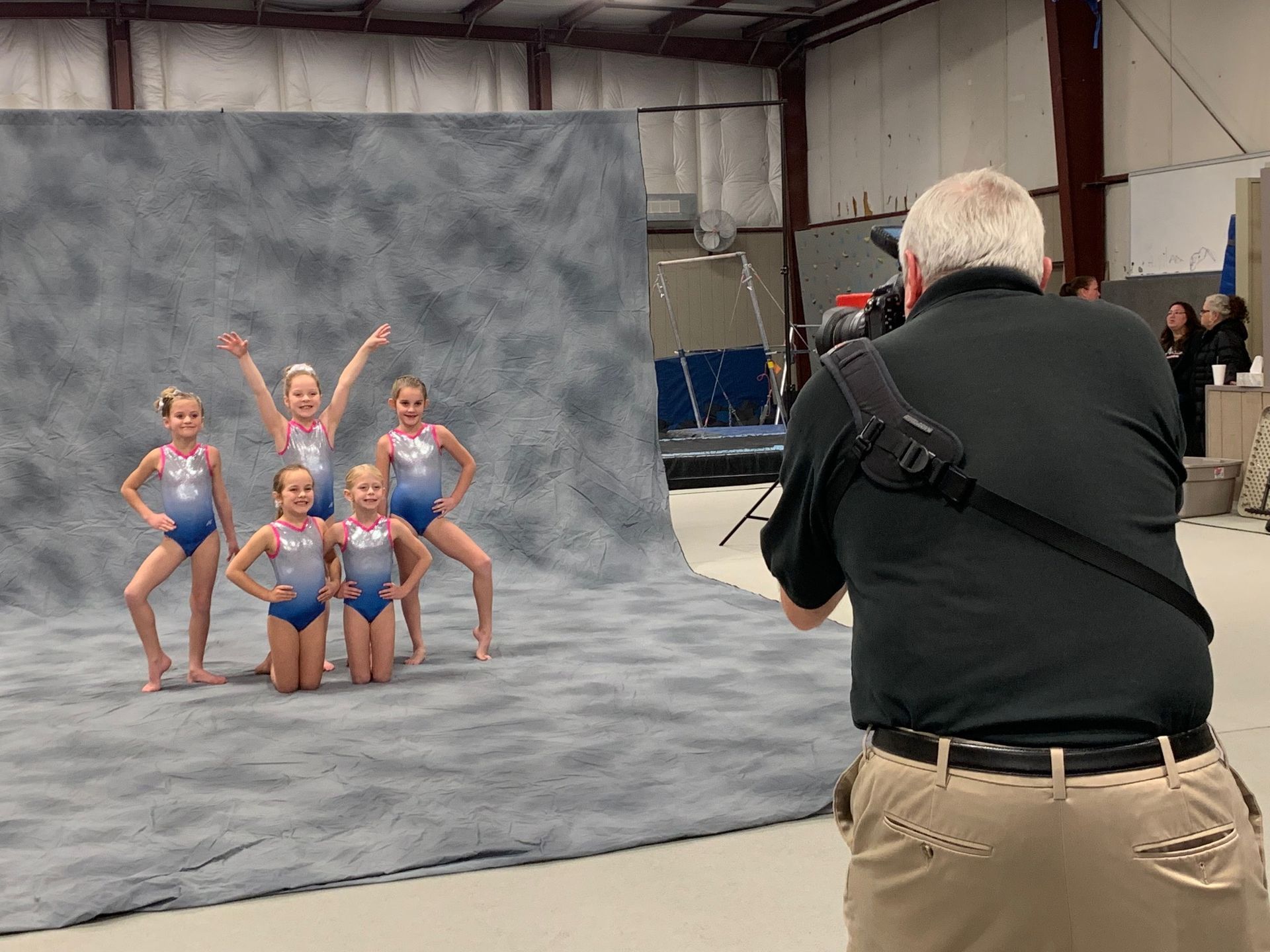 Photographer capturing a group of young dancers posing in blue costumes before a gray backdrop