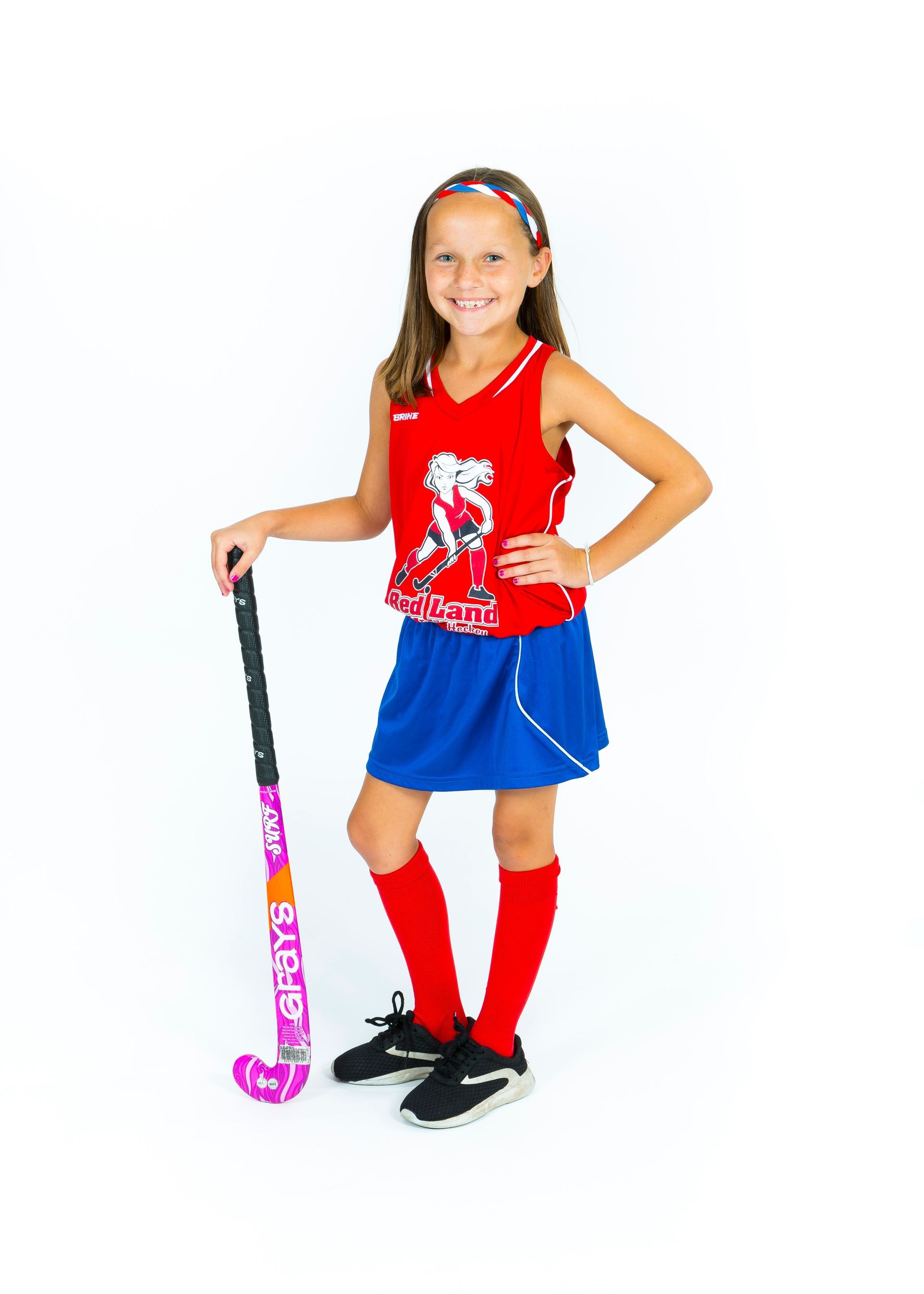 Child in red top and blue skirt holding a pink hockey stick, standing on a white background.