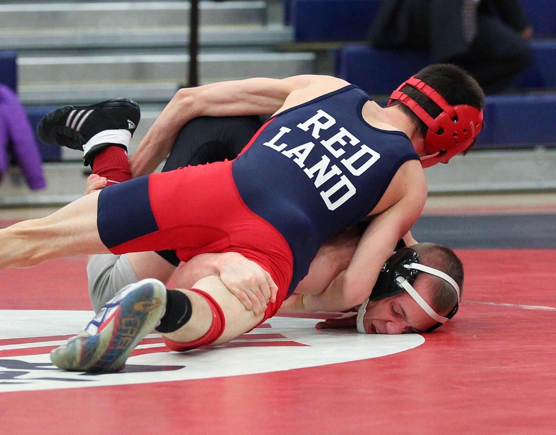 Wrestlers in red and blue uniforms grapple on a mat during a match