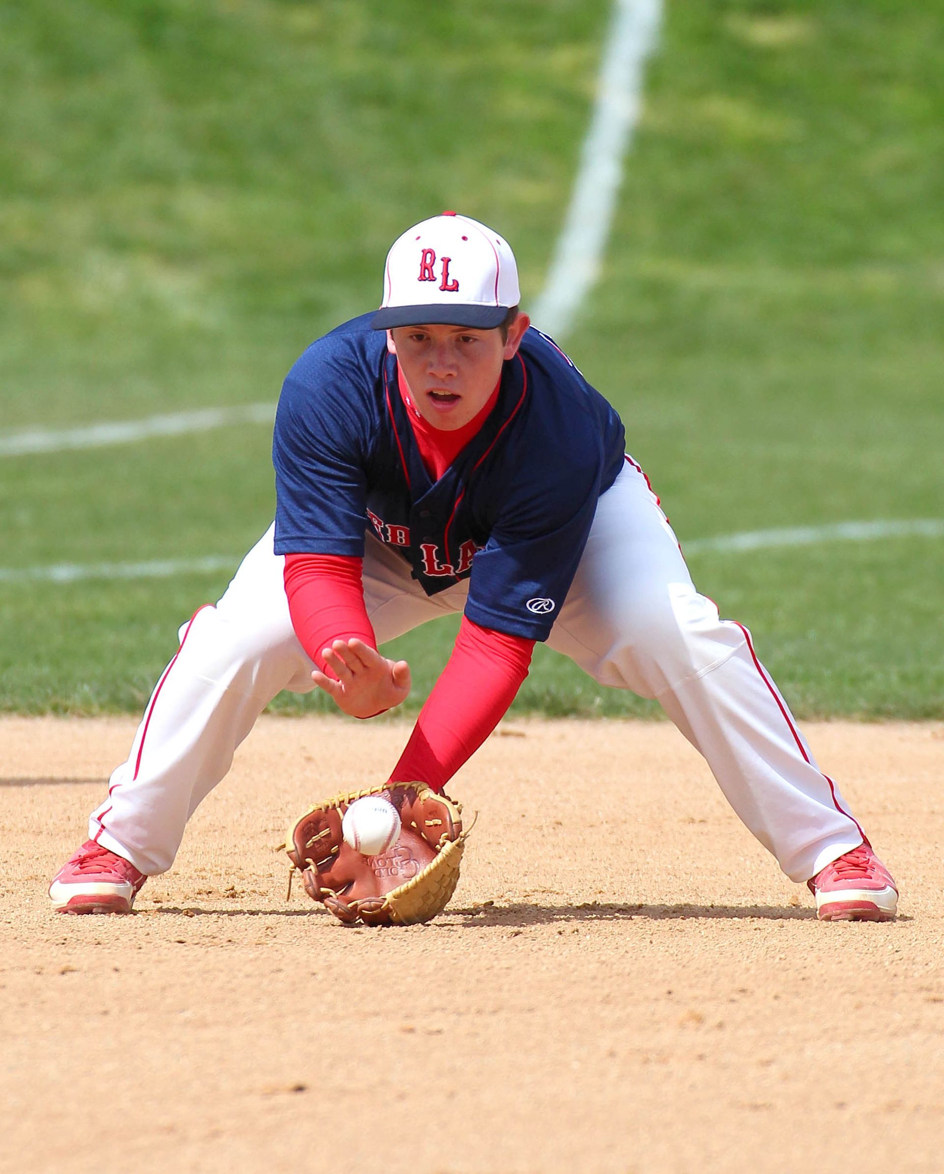 Baseball infielder in blue and red uniform fielding a ground ball on the infield dirt.