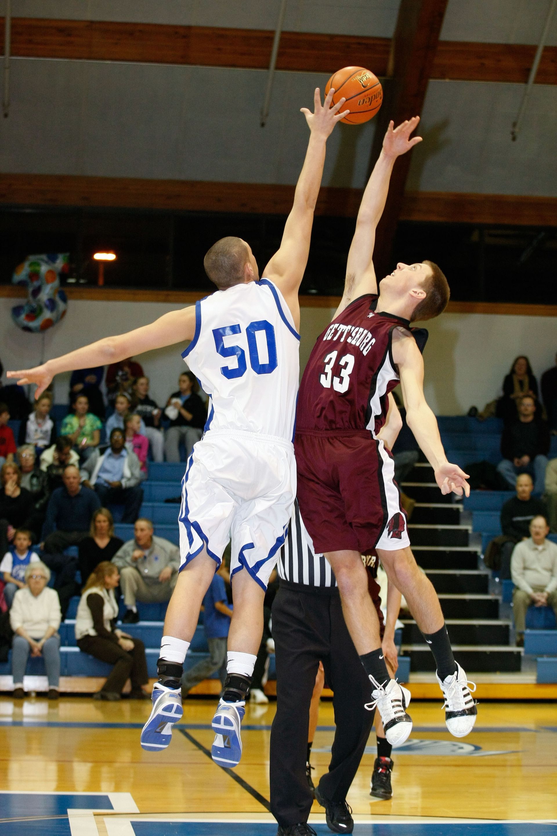 Two basketball players jump for a tip-off, reaching for the ball at center court