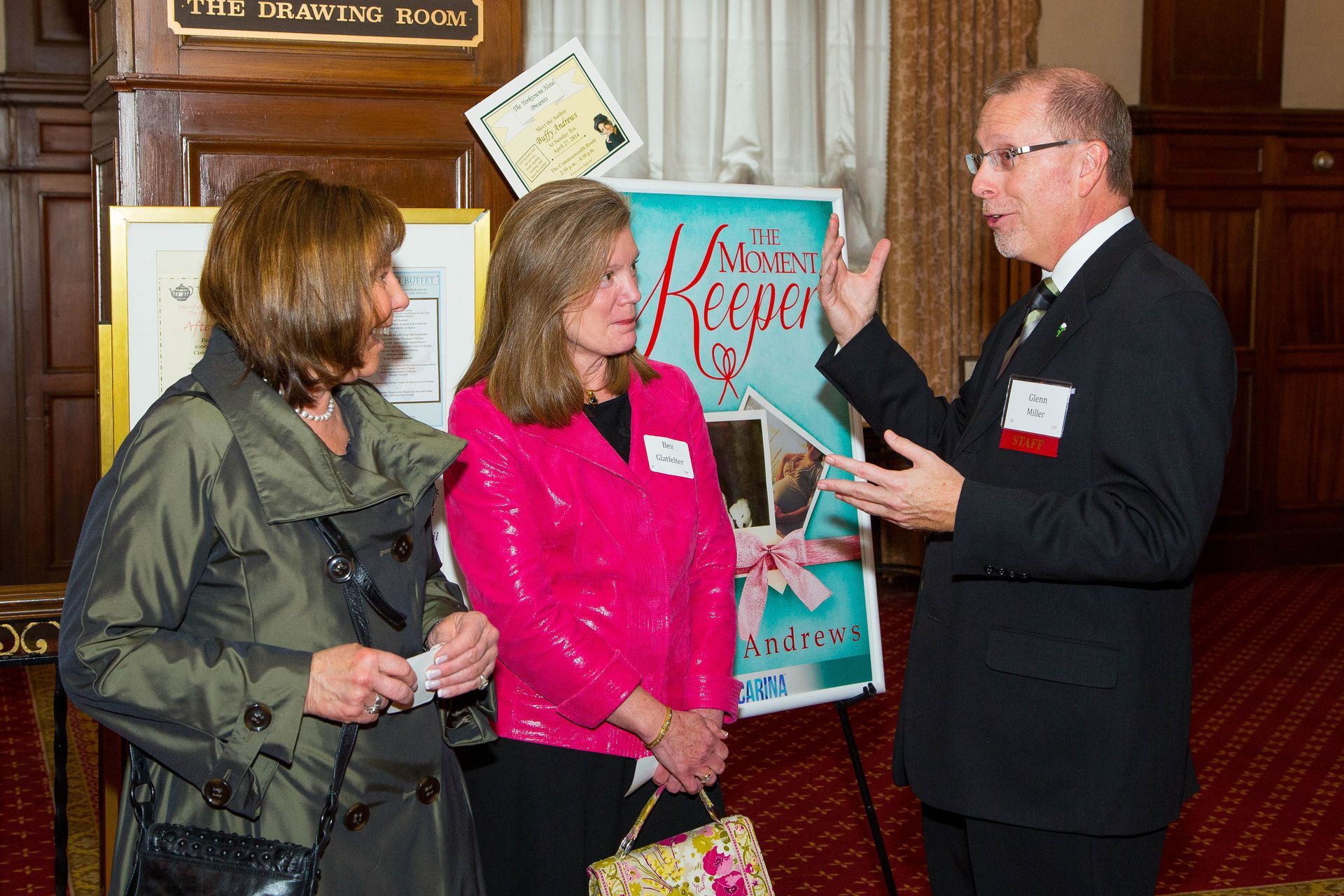Three people talk at an indoor event, with a poster board in the background.