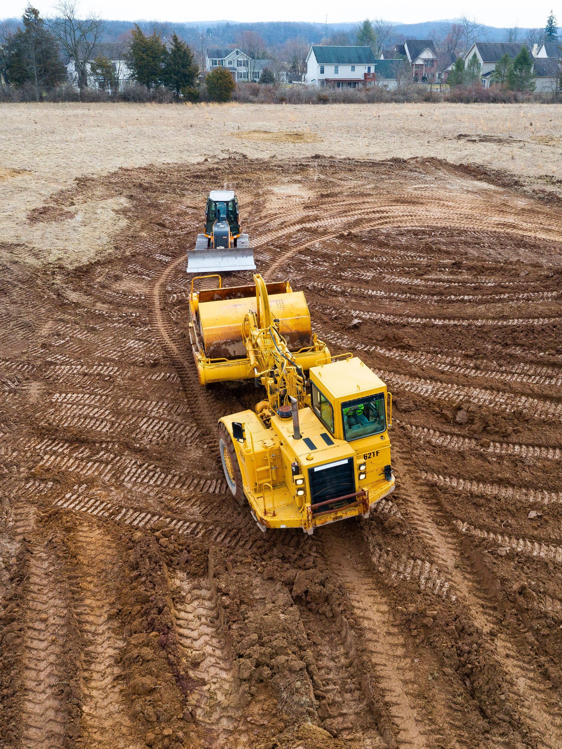 Yellow bulldozers grading a dirt field, with a blue tractor in the background.