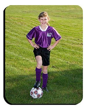 Young soccer player in purple jersey standing with one foot on a soccer ball on grass field