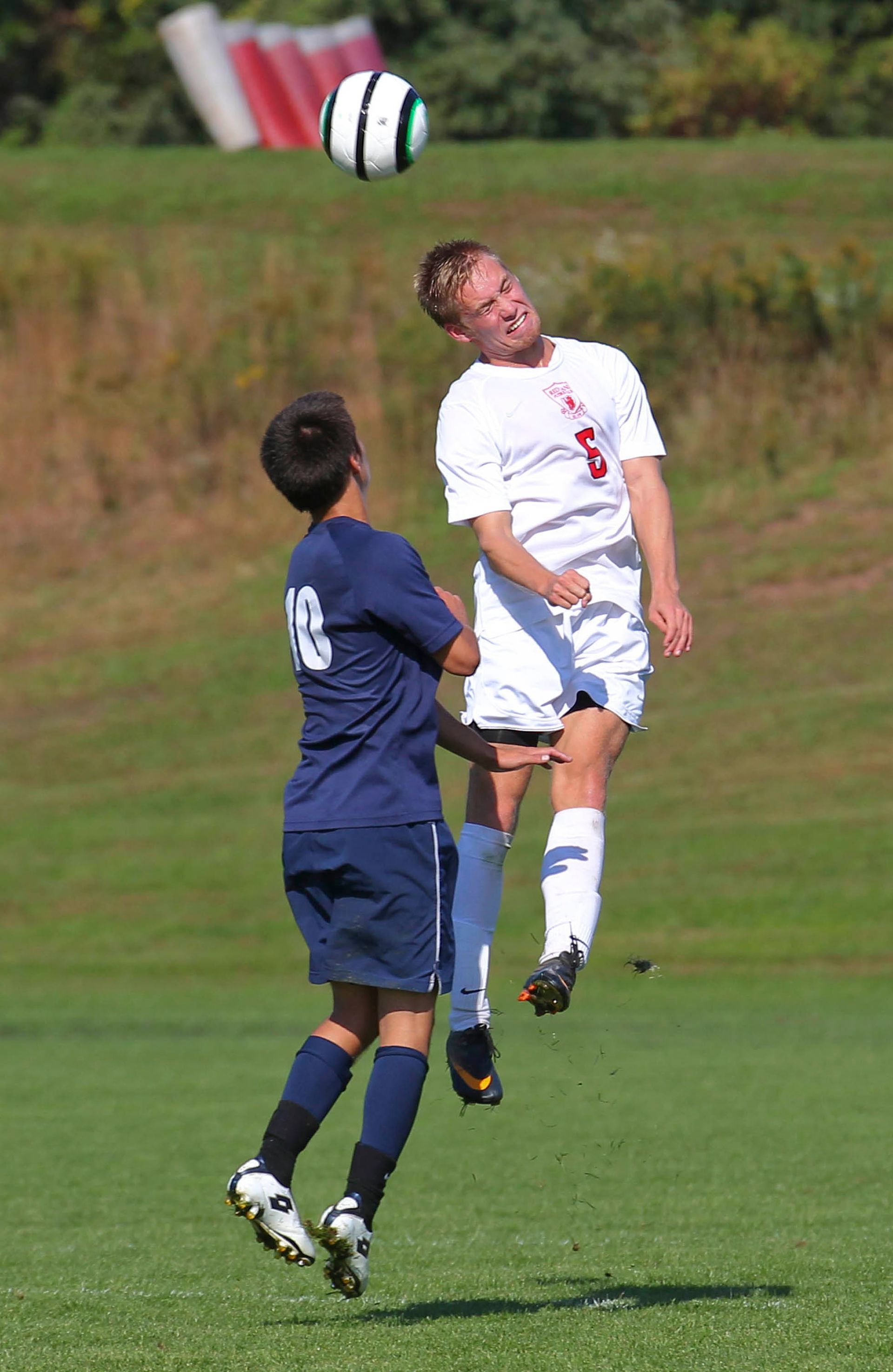 Two soccer players jump for a header on a grassy field, eyes on the ball.