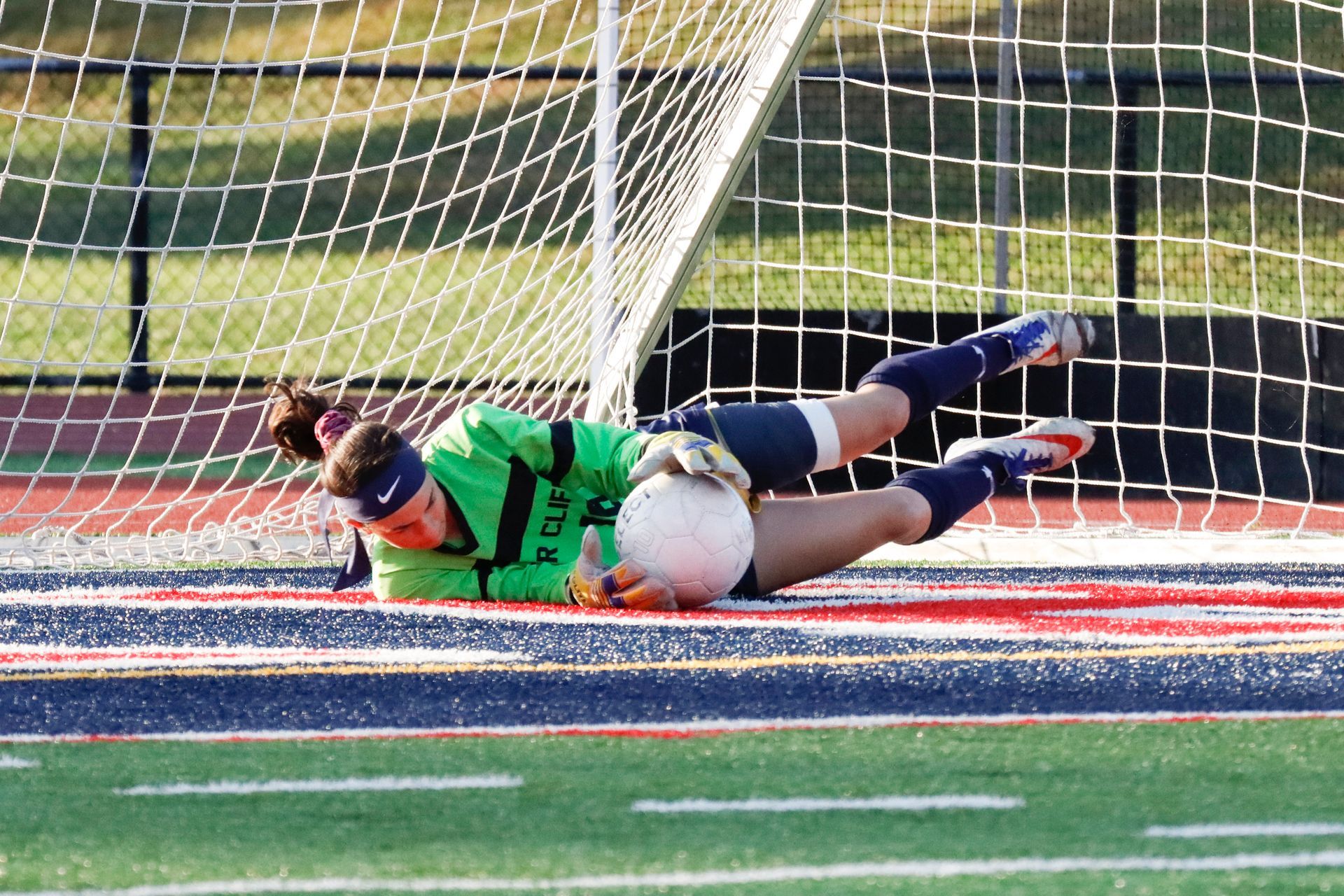 Soccer goalkeeper diving on the field, stretching to stop a ball near the goal line