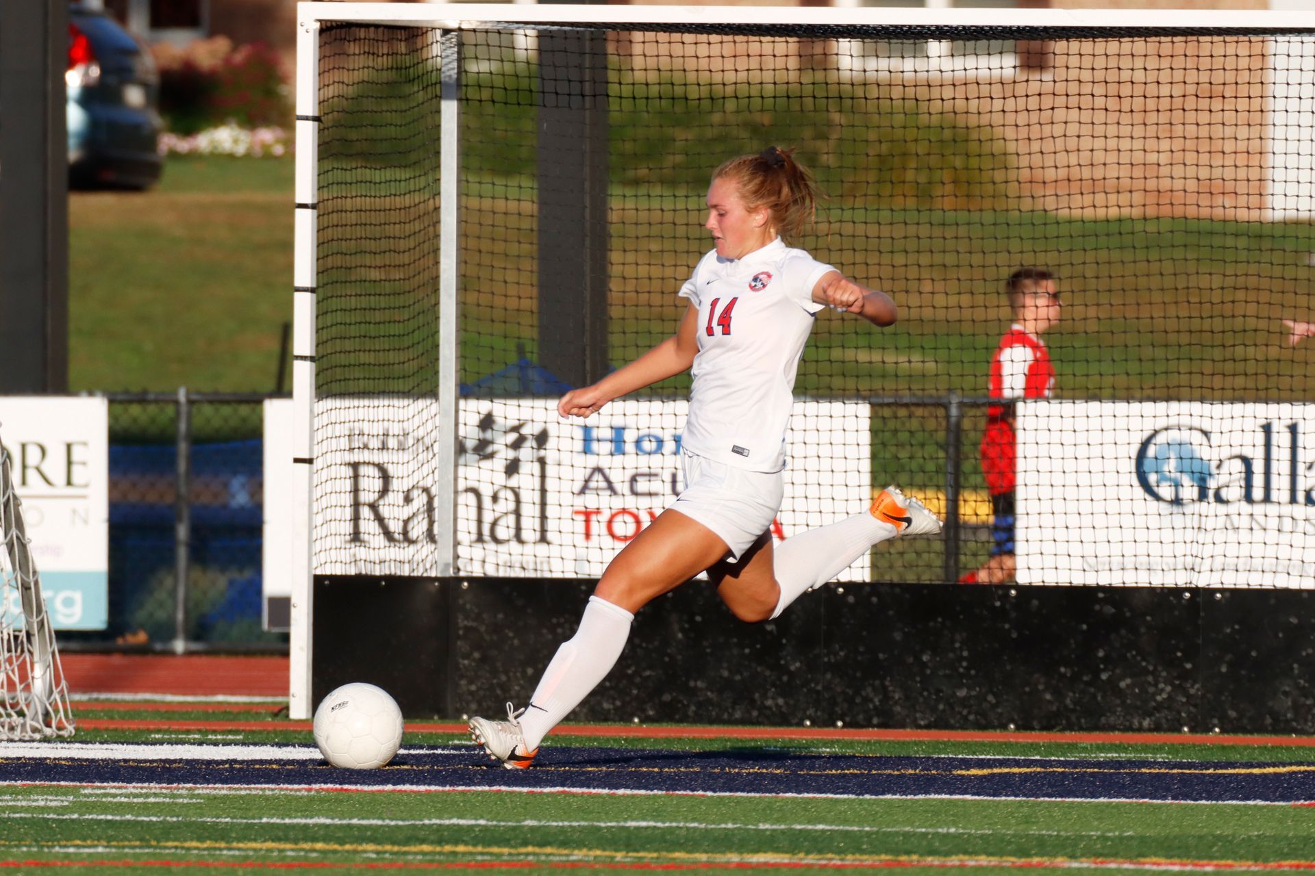 Soccer player in white kicks a ball on a field near the goal