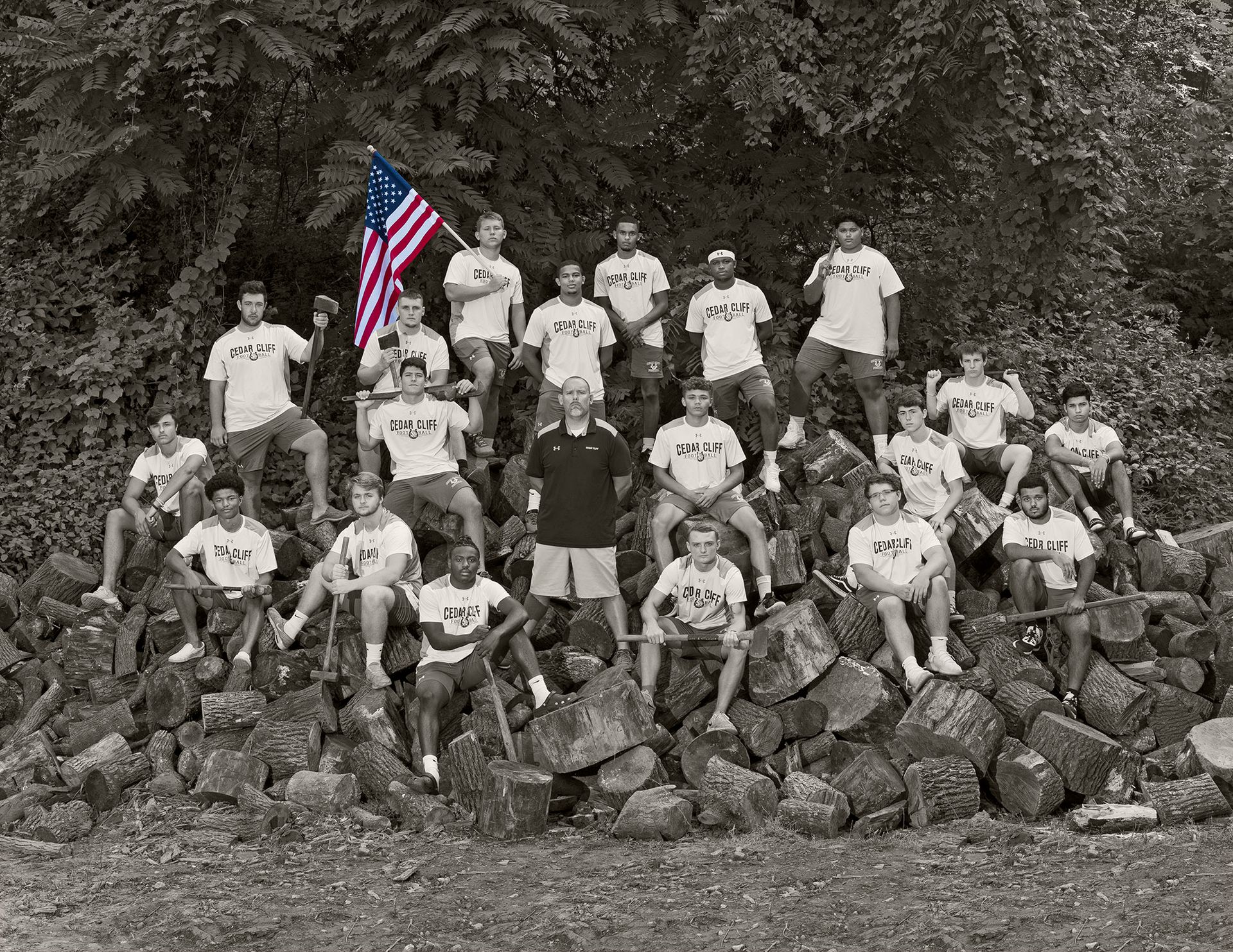 Large group posing on rocky hillside; one person holds an American flag in front of trees.