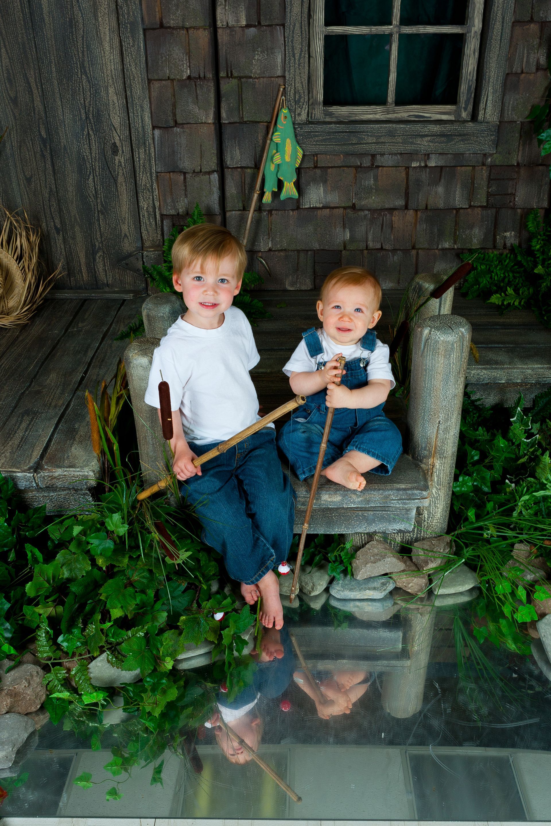 Two children sitting on a rustic chair outside a weathered wooden cabin, one holding a stick.