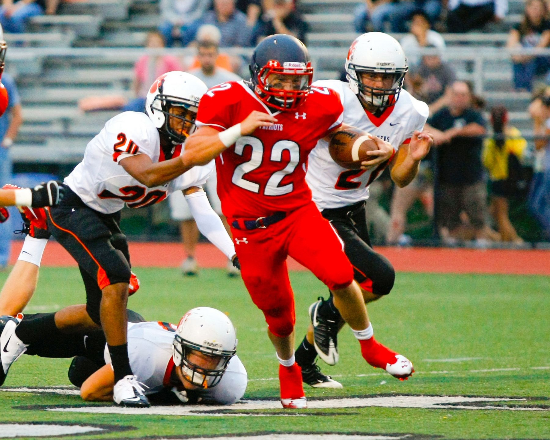 College football player in red jersey runs with the ball as defenders tackle on the field