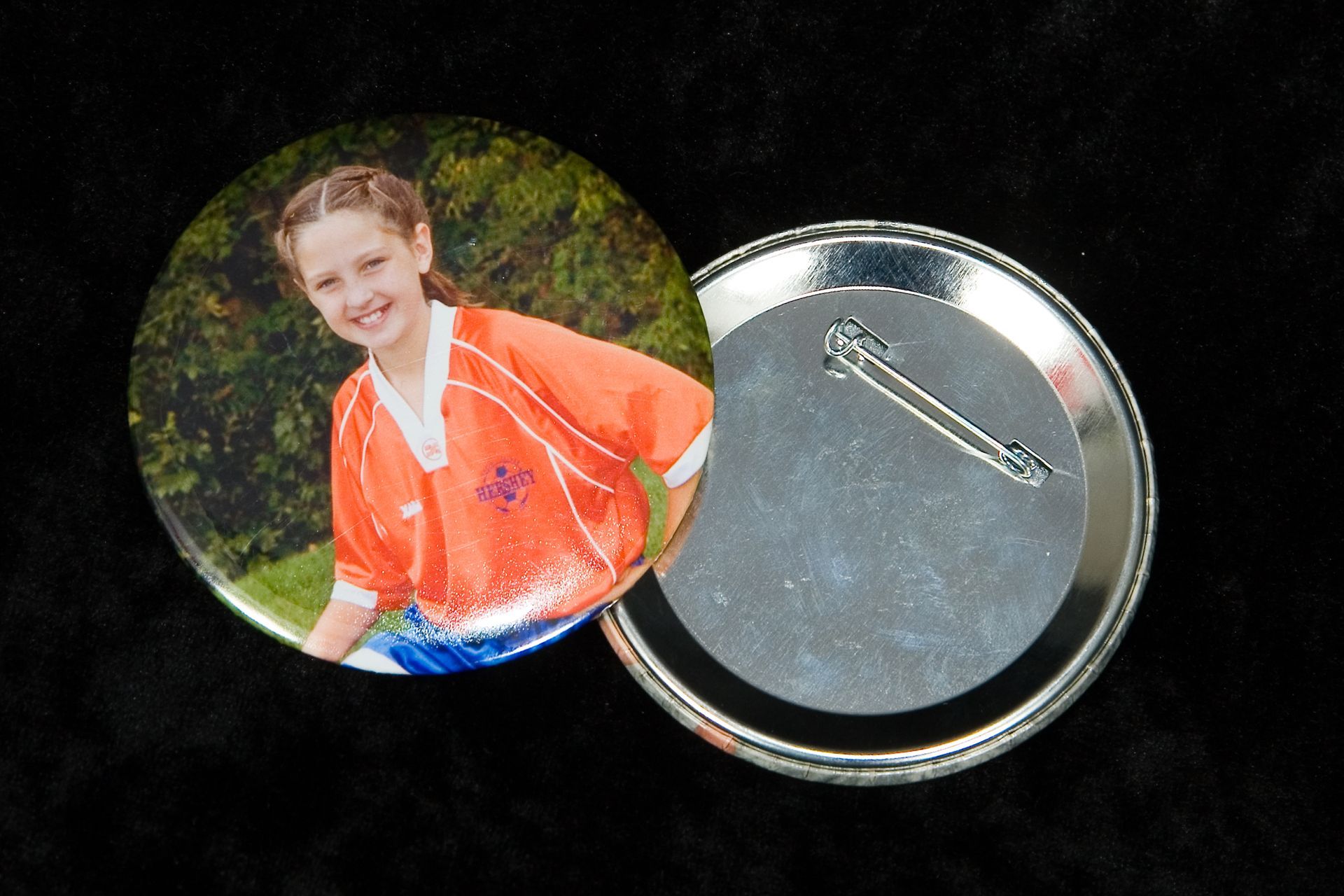Round photo pin button with a smiling person in an orange shirt on the front and a safety pin on the back
