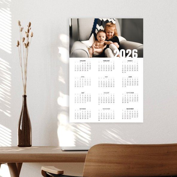 2026 wall calendar with a family photo hanging above a desk in a bright room