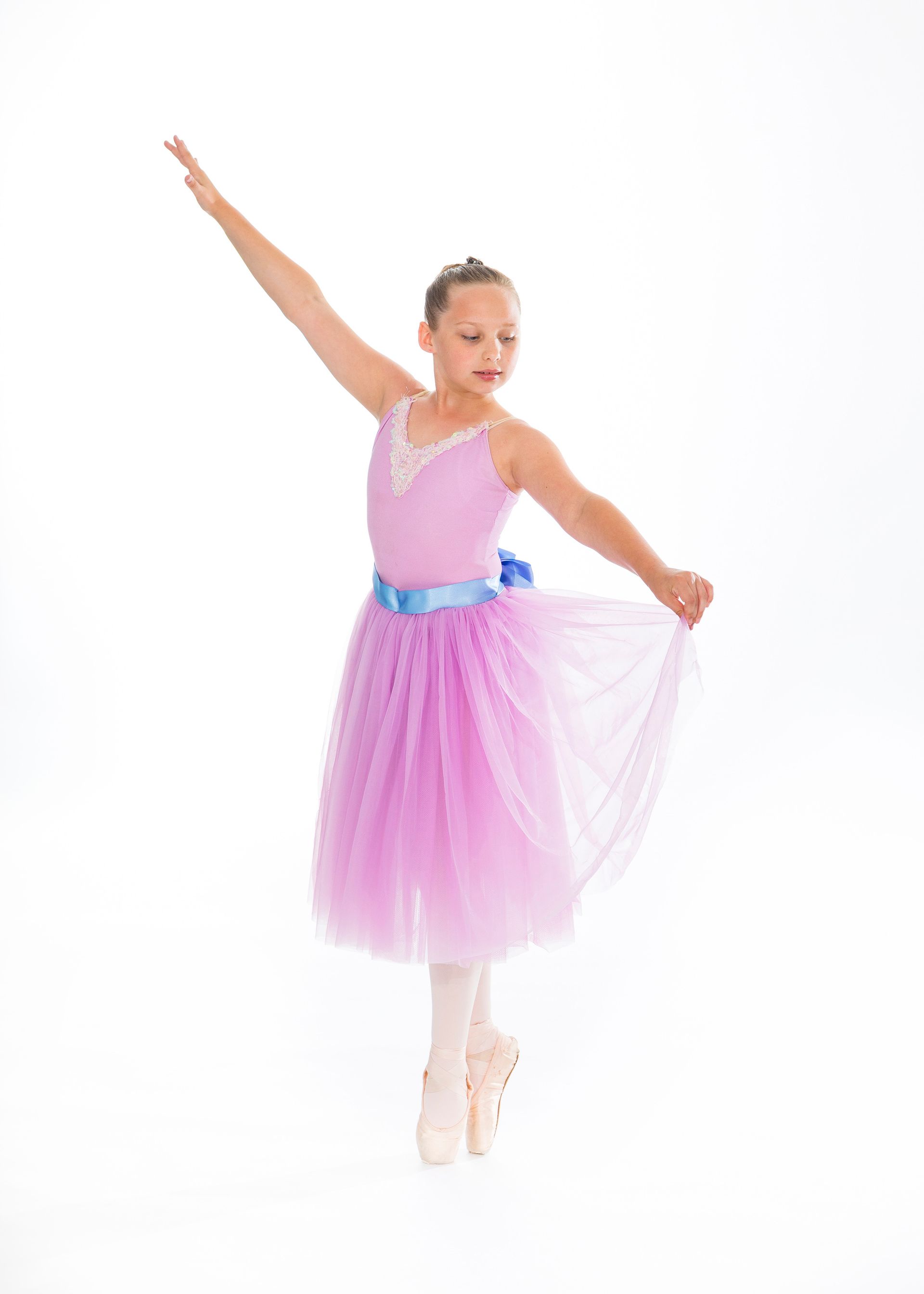 Young ballet dancer in a pink tutu posing with one arm raised on a white background