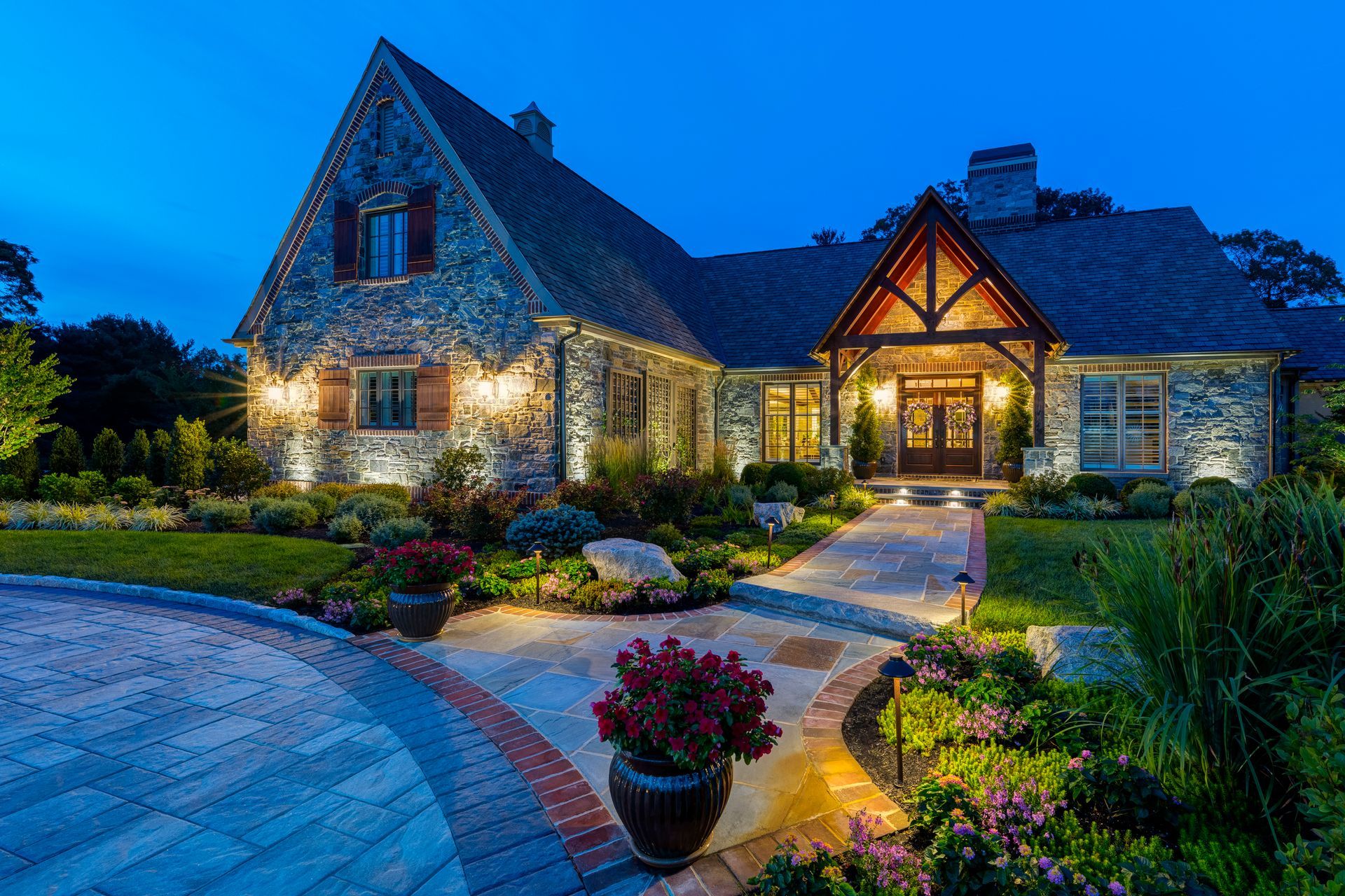 Stone house at dusk with lit windows, arched entry, and a landscaped garden path.