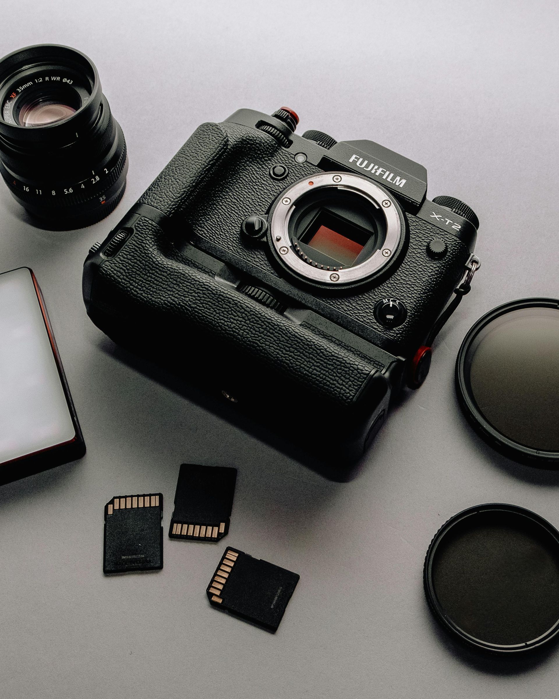 Black digital camera with detached lens, cap, filters, and memory cards on a white surface