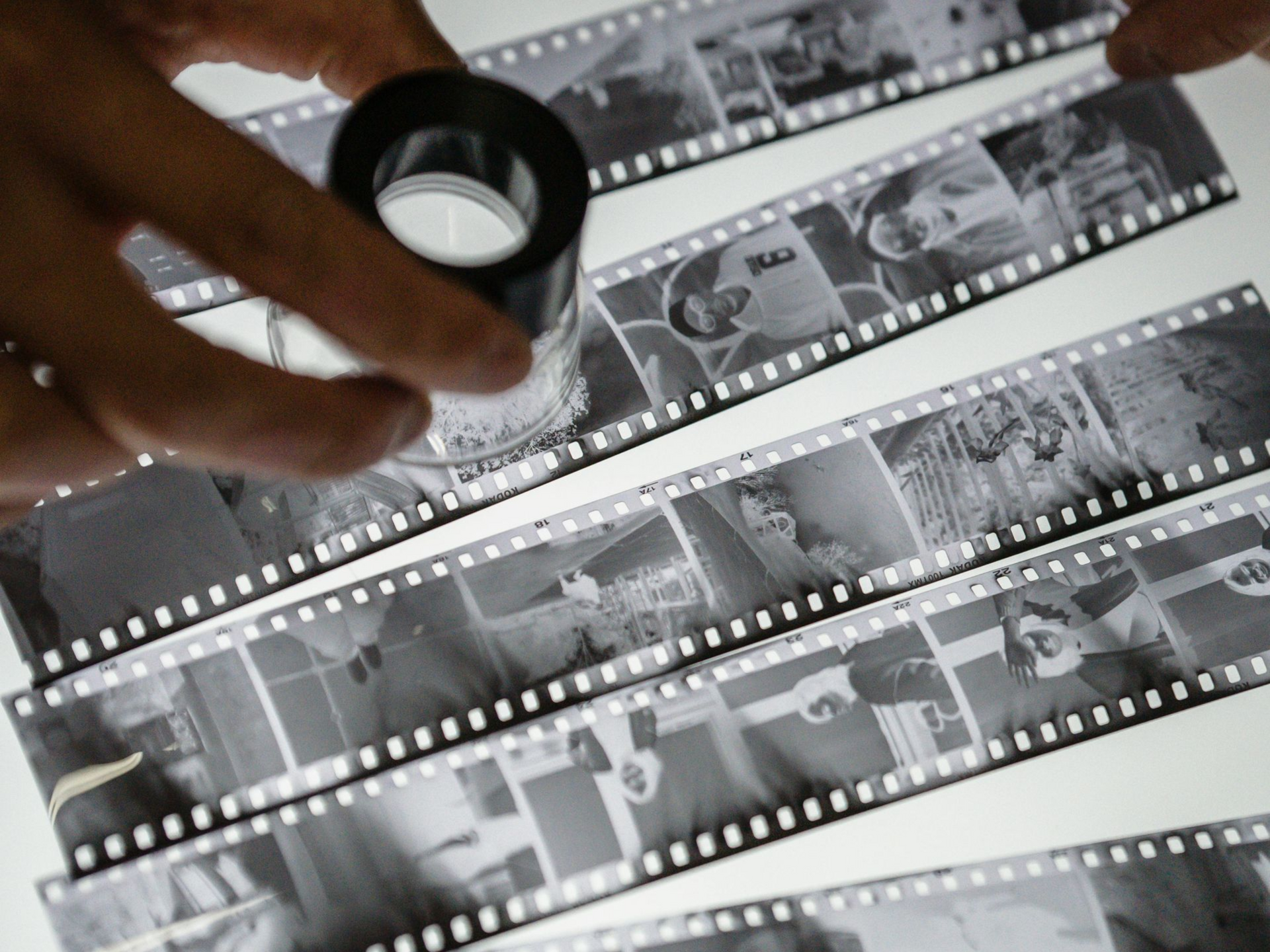 Hand holding a magnifying glass over black-and-white film negatives on a light table