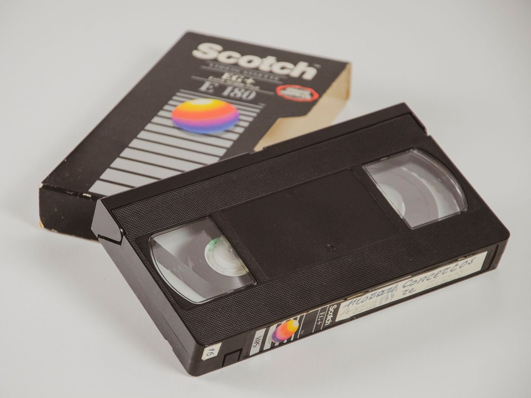 Two VHS tapes, one partially in its black case, with a colorful label behind it