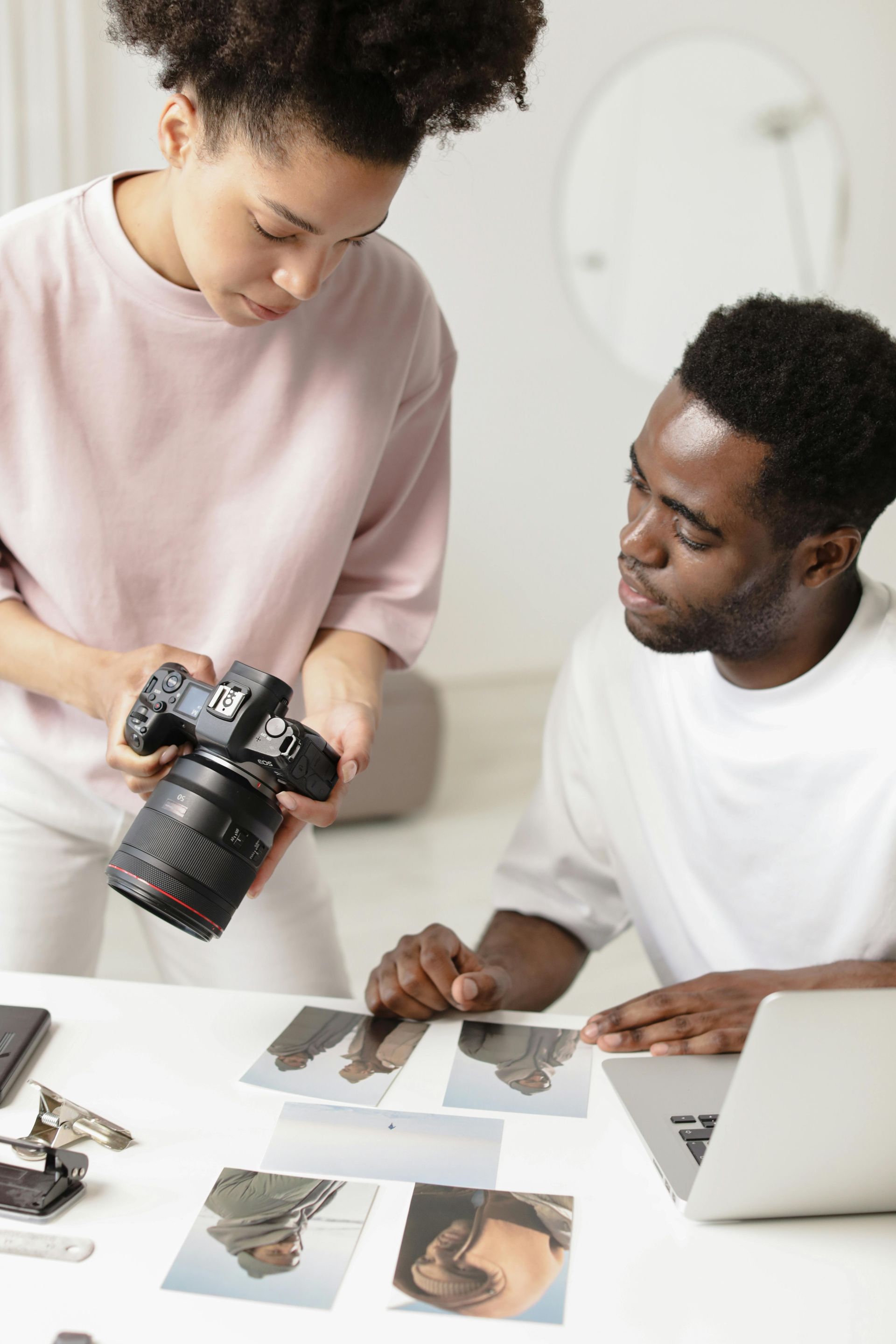 Two people reviewing printed photos on a table, one holding a camera in a bright studio