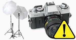 Vintage Minolta camera beside studio lights with yellow warning triangle overlay