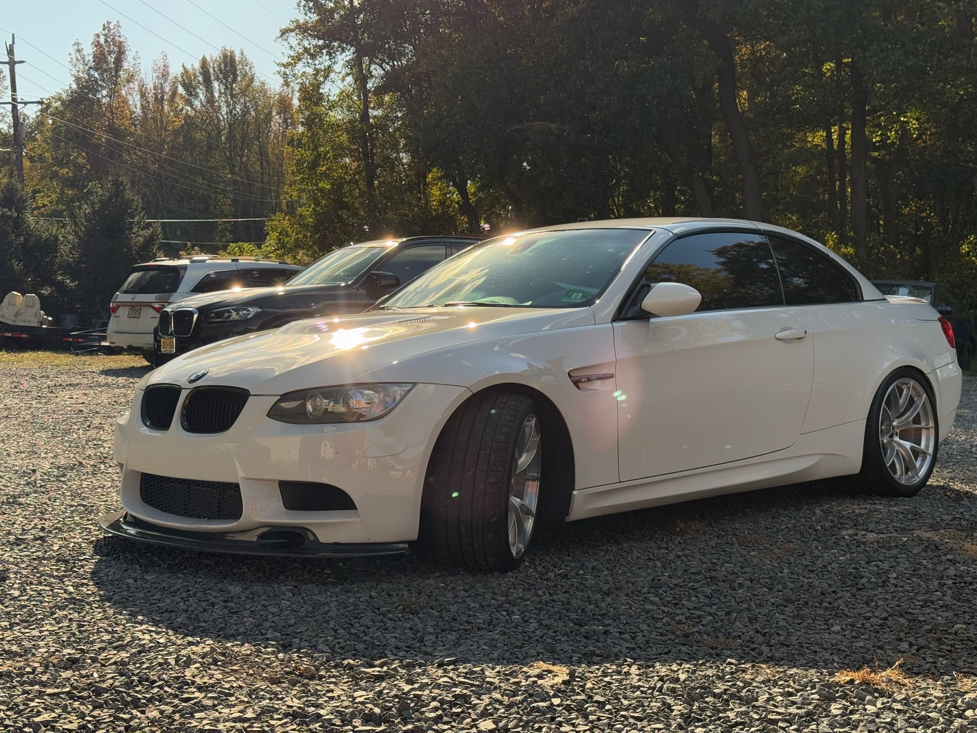White BMW coupe parked on gravel in a sunny lot with trees in the background