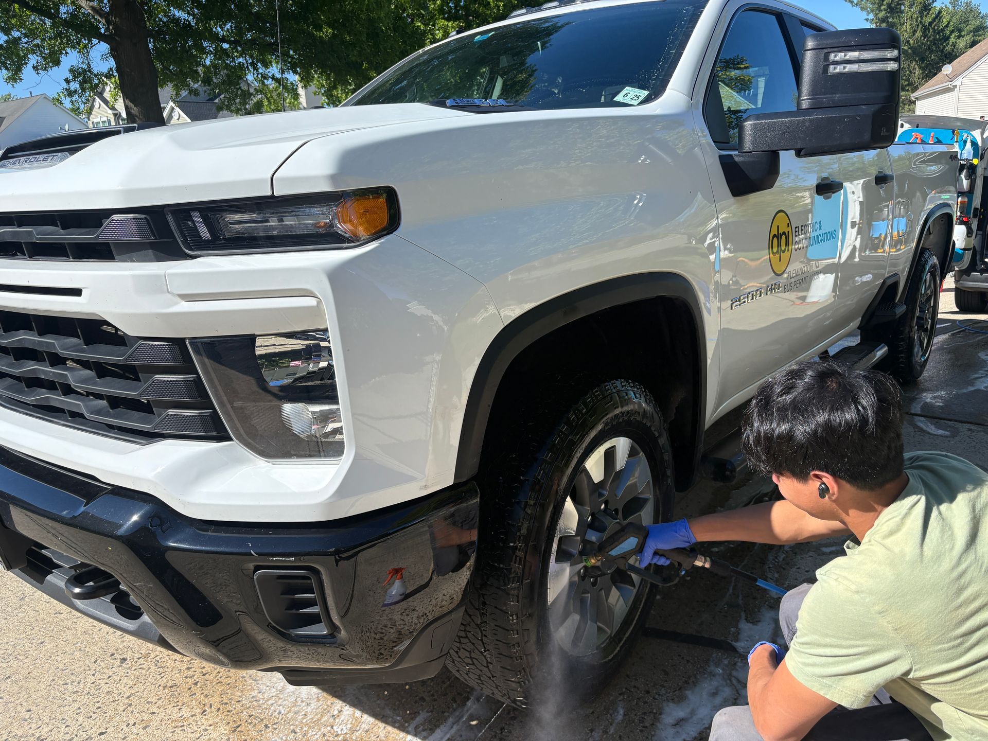 Person polishing a white pickup truck’s wheel in a sunny parking lot