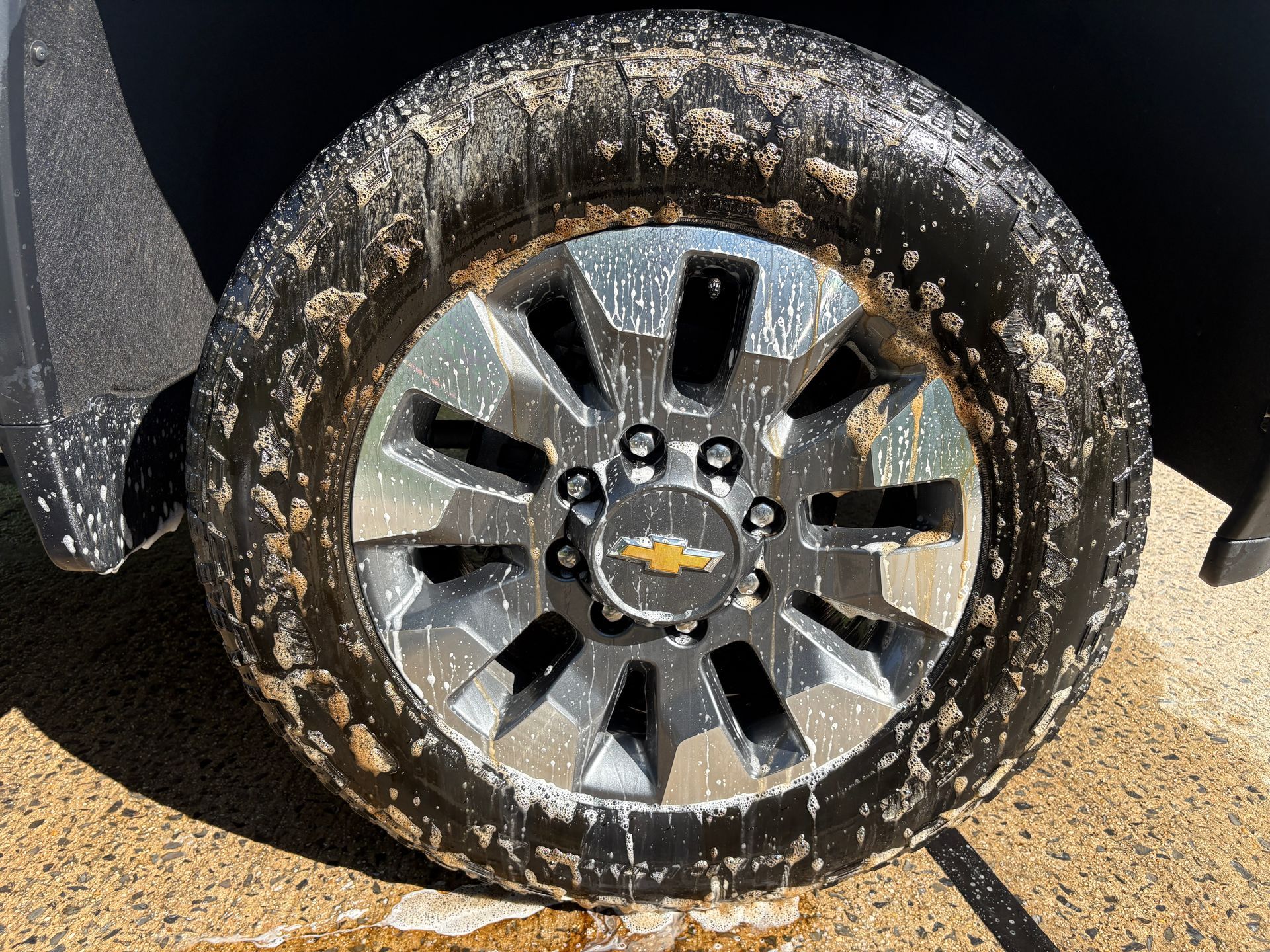 Close-up of a muddy Chevrolet truck wheel with silver rim on pavement.