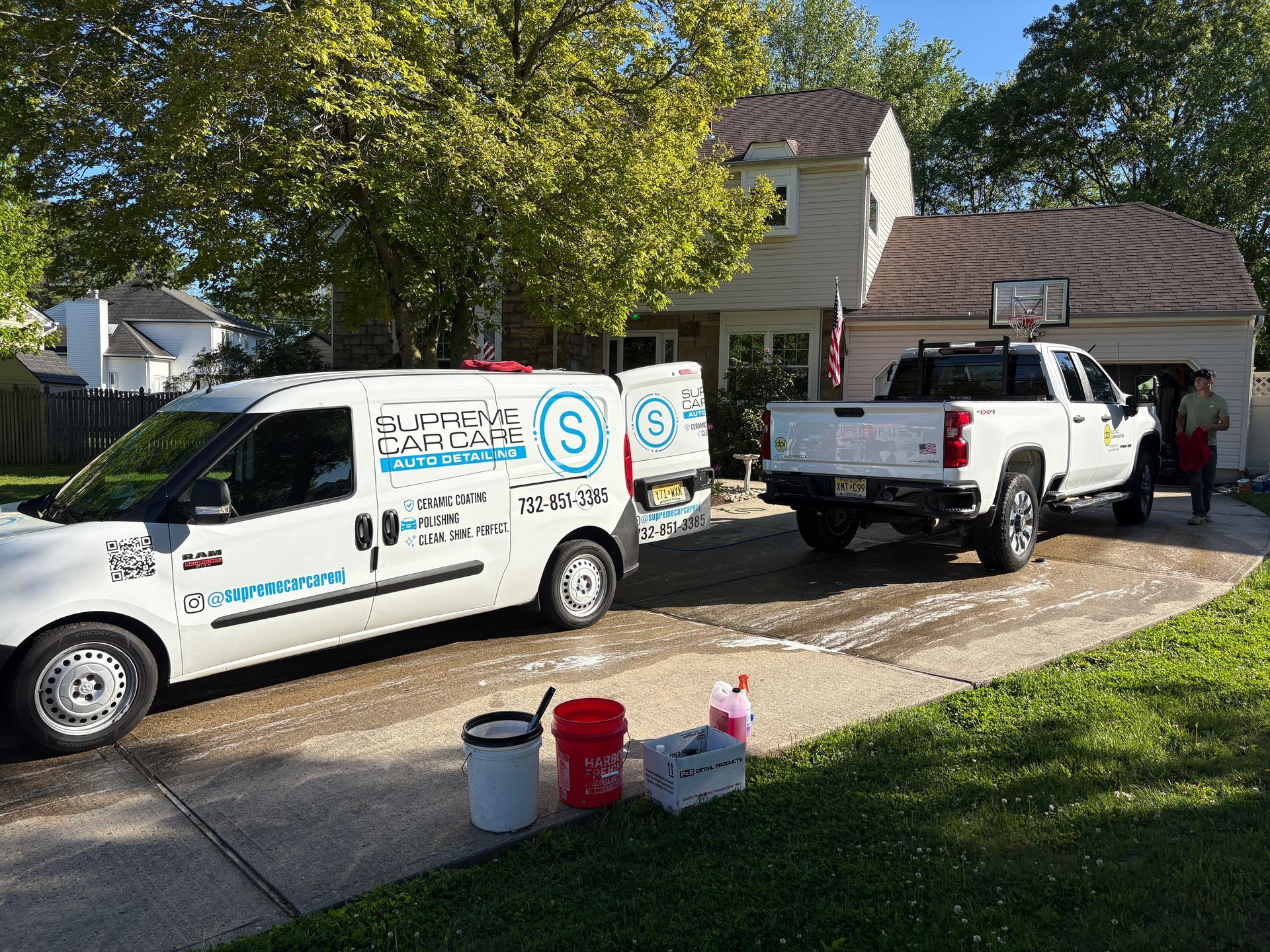 Two white service vans parked in a driveway with a worker by the rear truck.