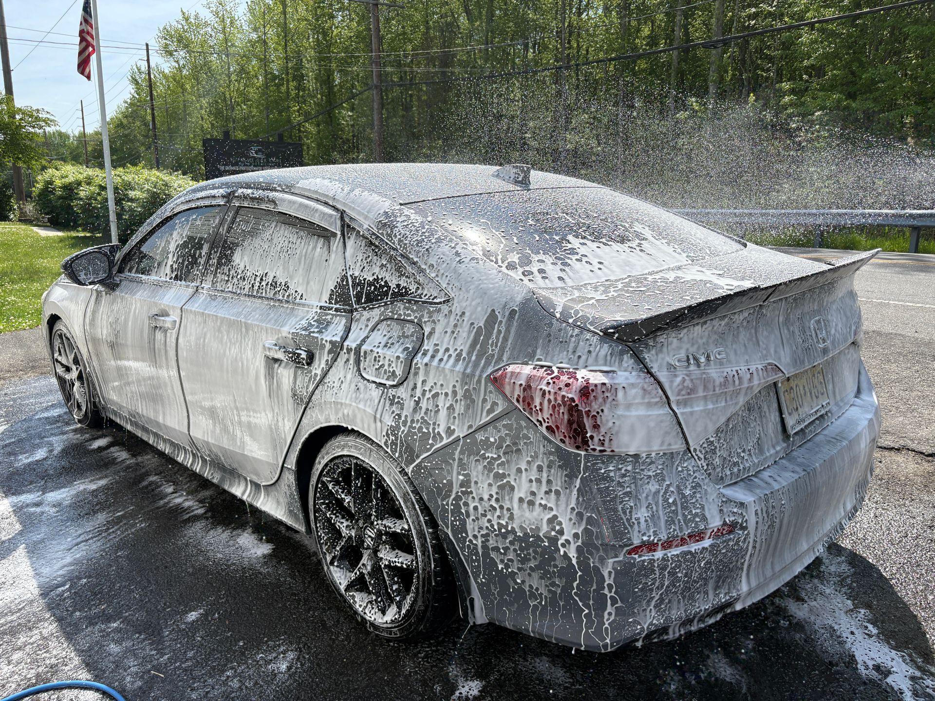 Car covered in white foam being rinsed with water on a sunny driveway