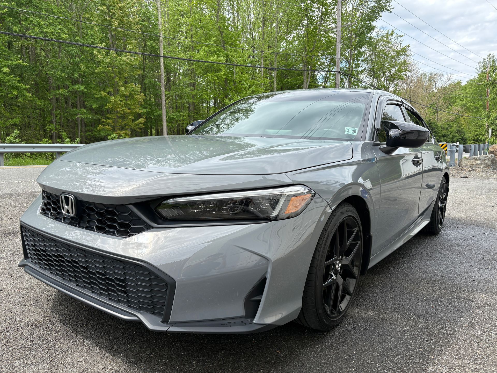 Silver Honda sedan parked on wet pavement beside a wooded area