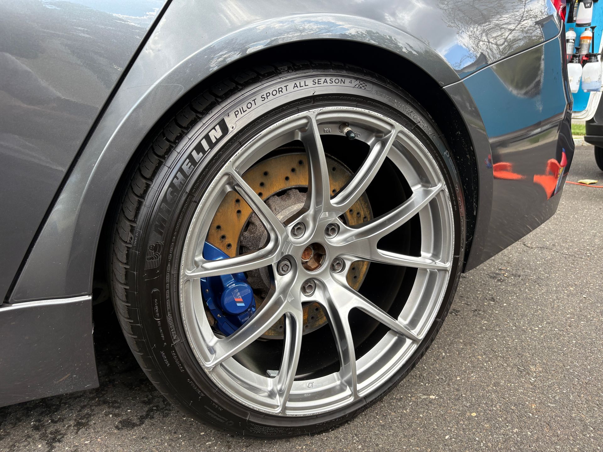 Close-up of a gray sports car’s front wheel with silver alloy rim and blue brake caliper.