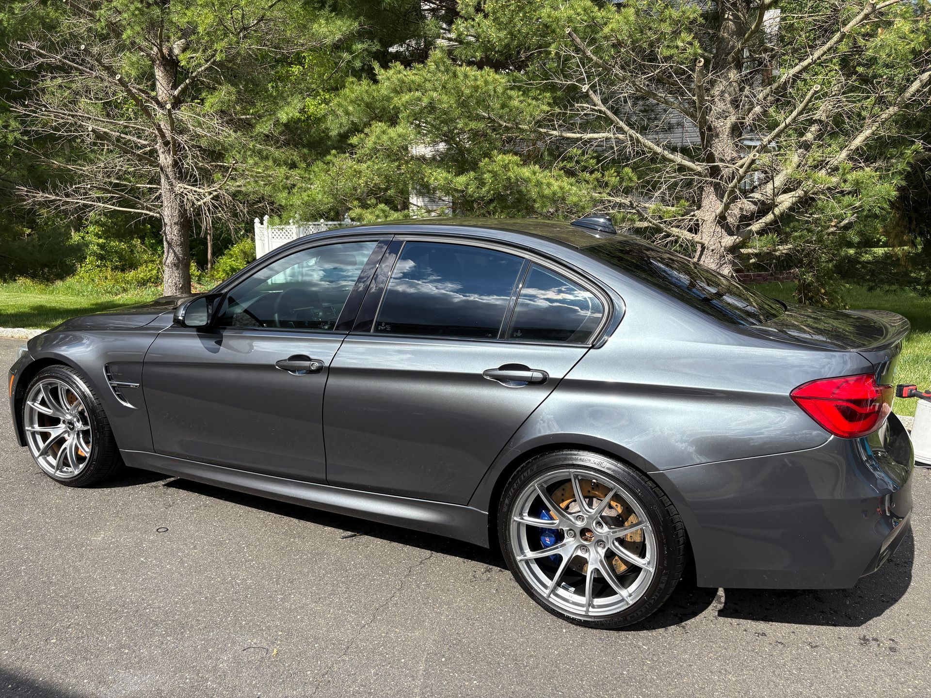Gray sedan parked on a road beside trees and greenery