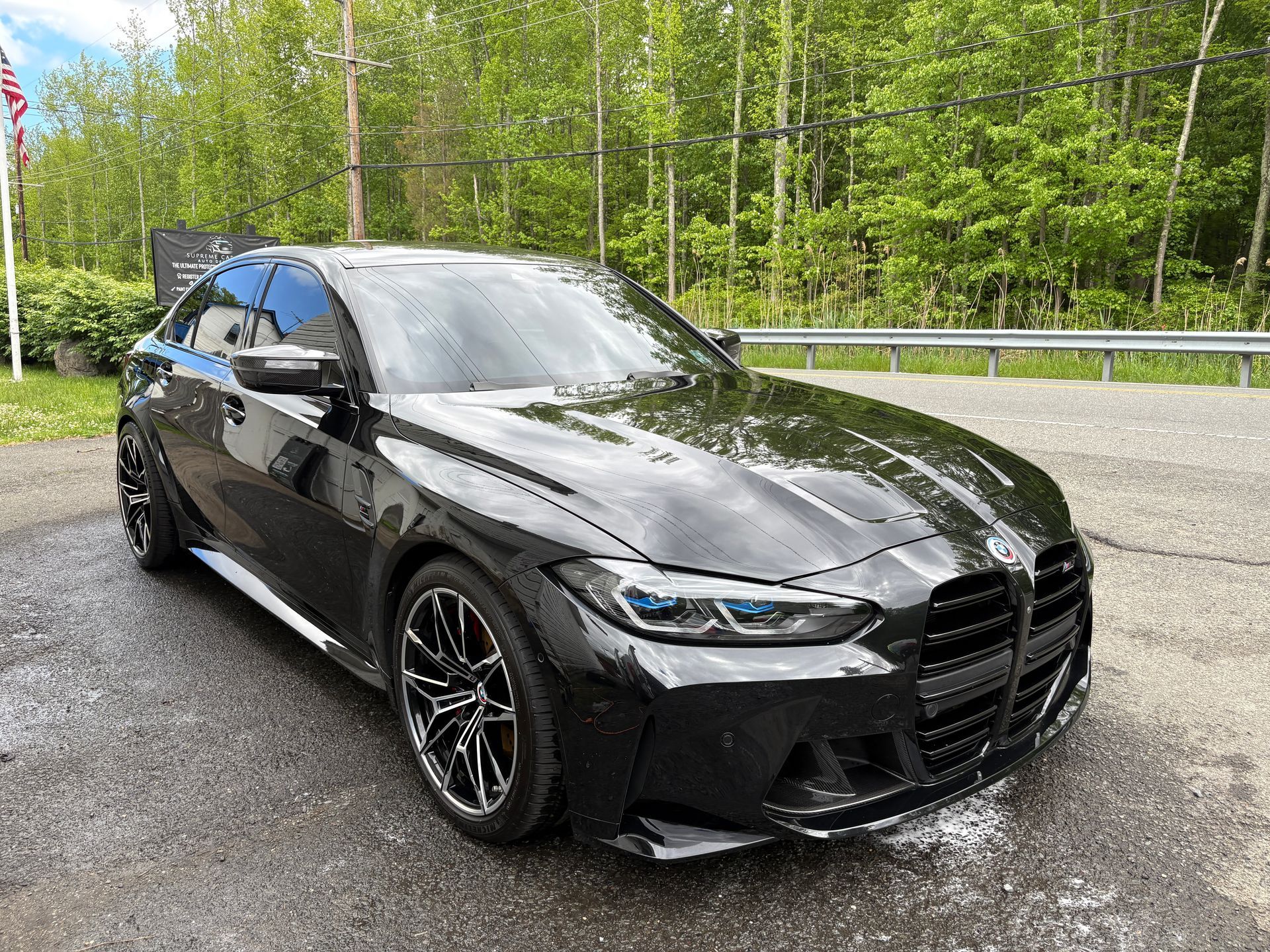 Black BMW sedan parked on a wet roadside with green trees in the background