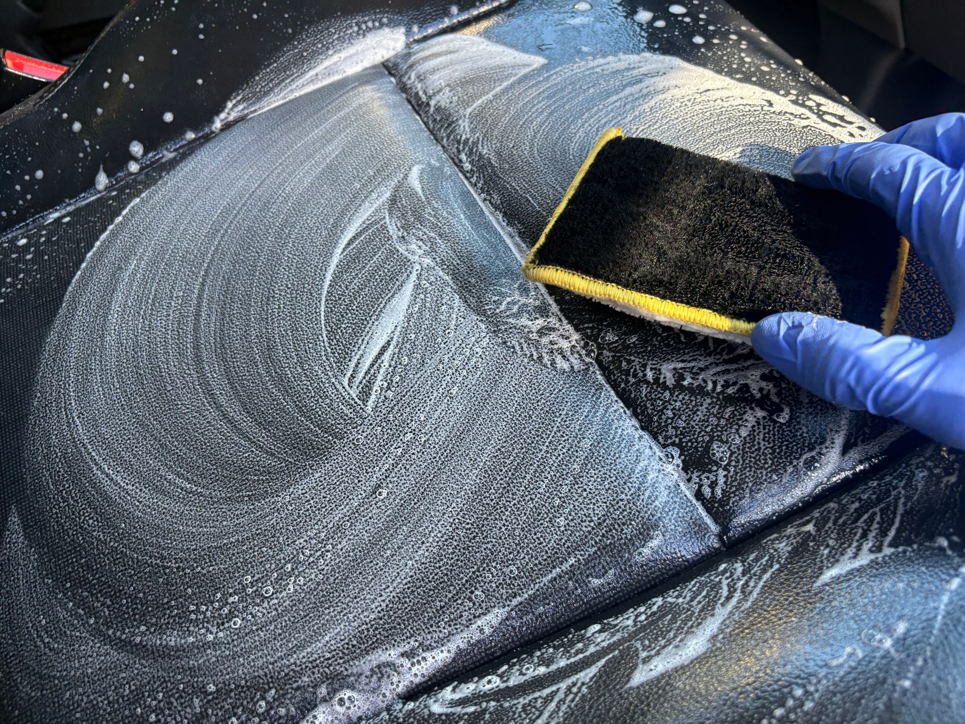 Gloved hand wiping dust from a dark car panel with a sponge
