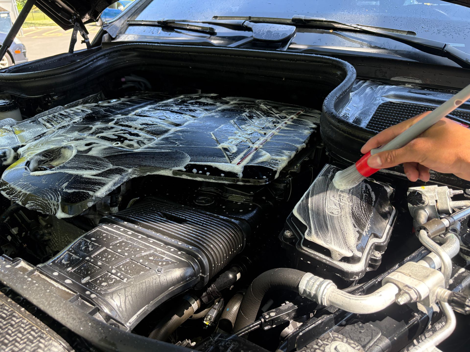 Person sprays water on a car engine bay covered in white foam.