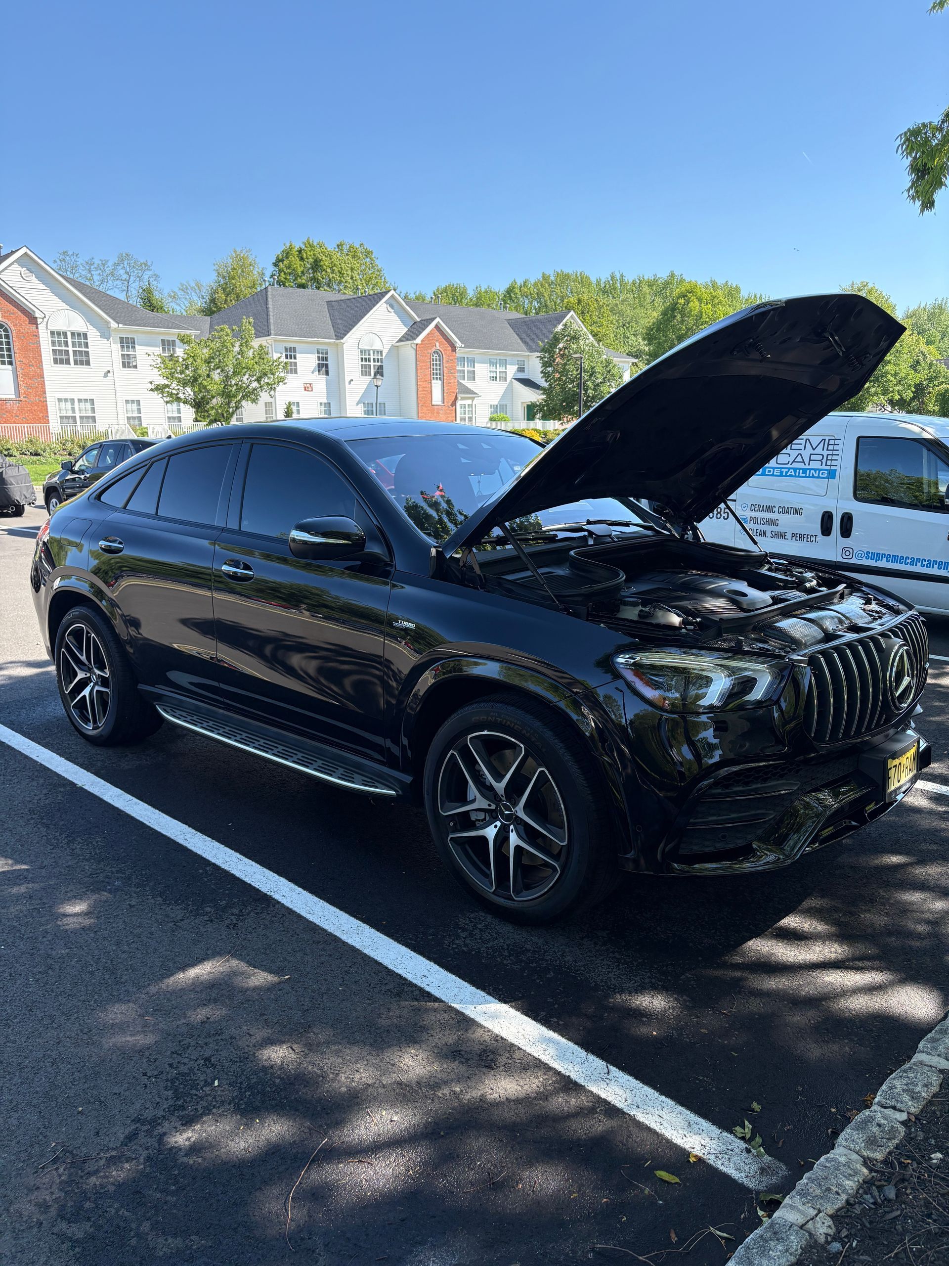 Black SUV with hood open parked in a lot on a sunny day.