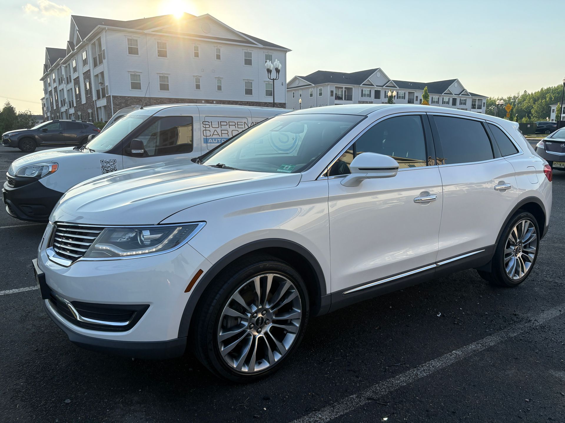 White SUV parked in a lot at sunset with apartment buildings in the background