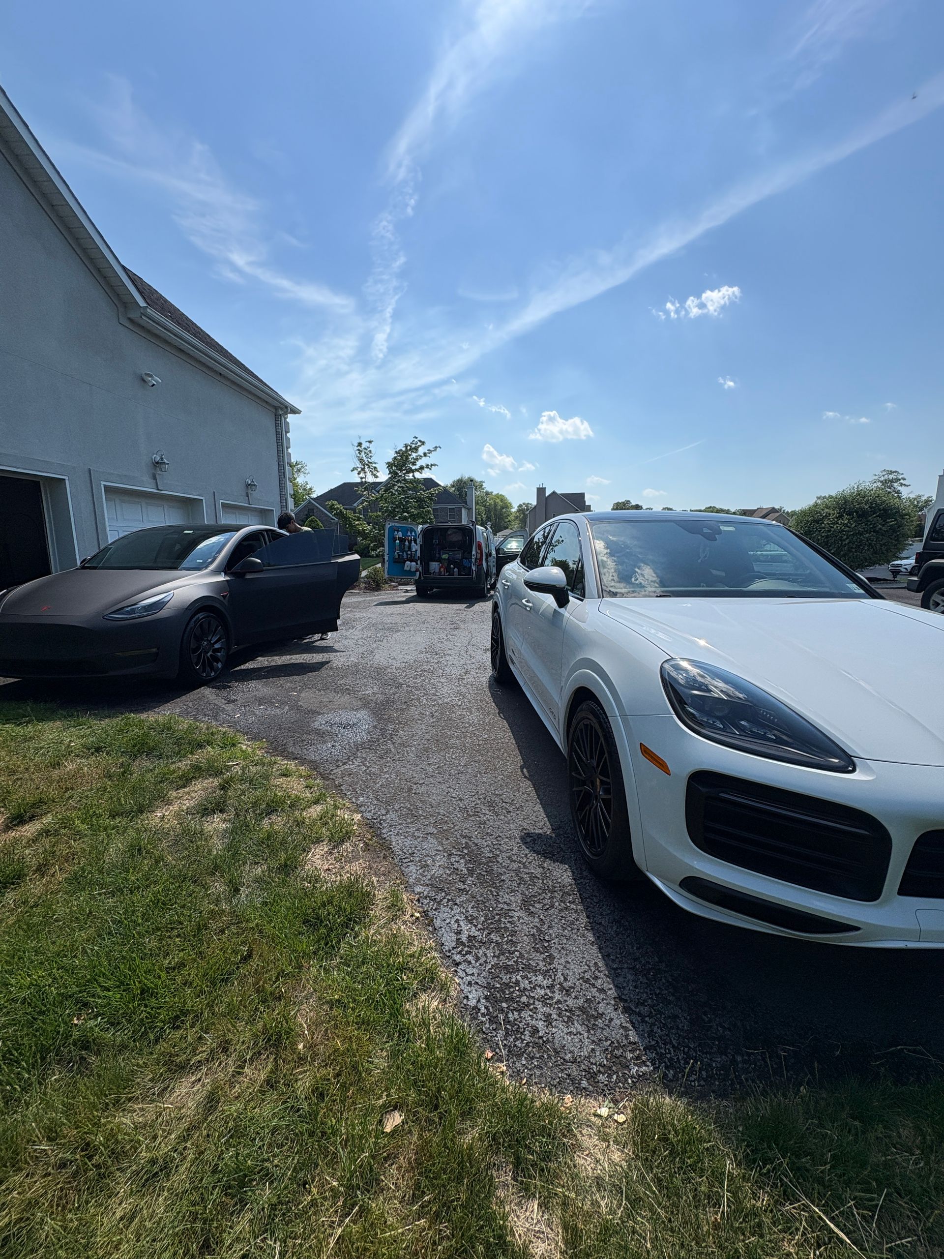 White convertible and black sedan parked on a gravel driveway beside a white building under a bright blue sky