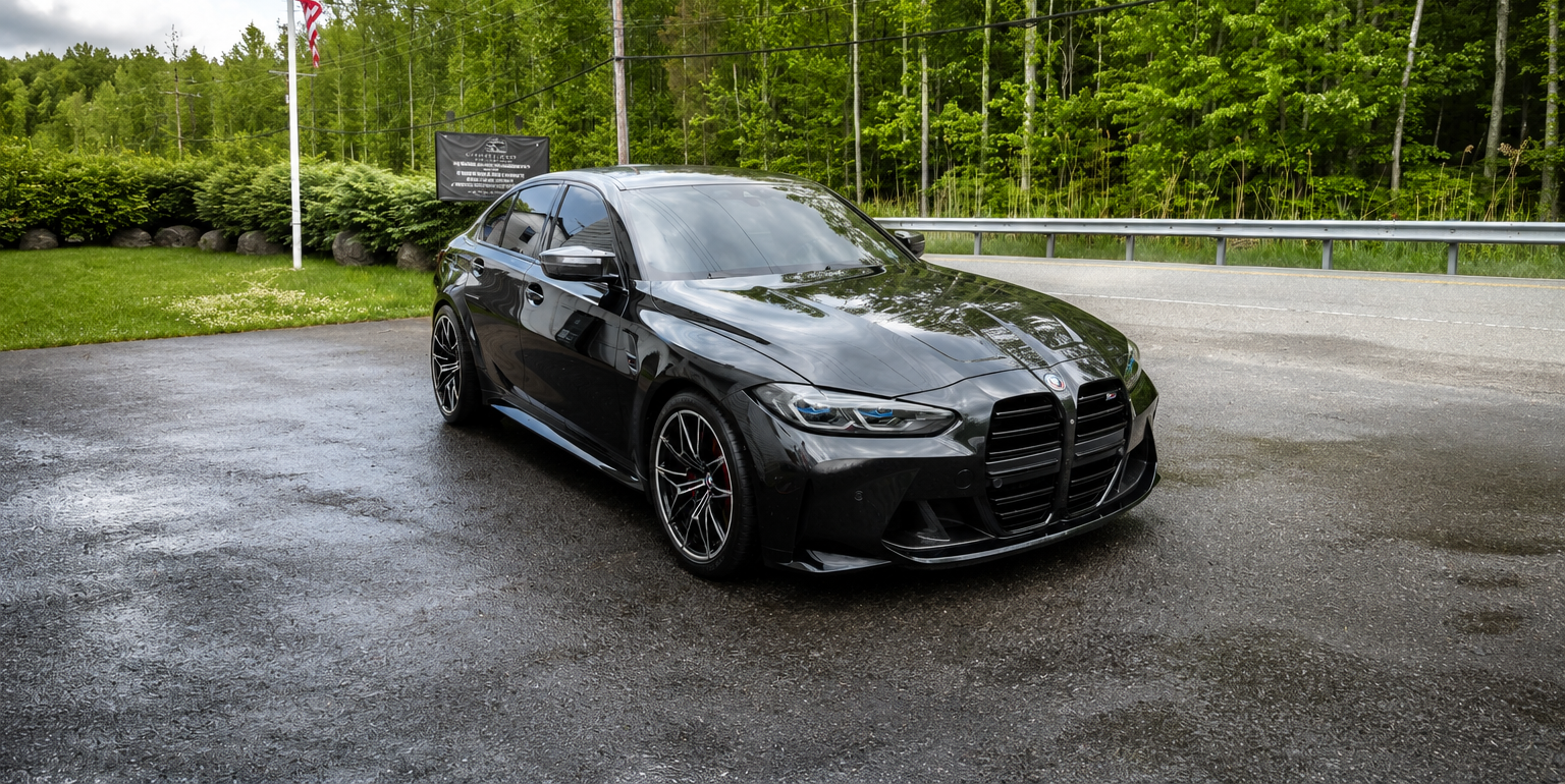 Black sports car parked on a wet roadside with trees and grass in the background