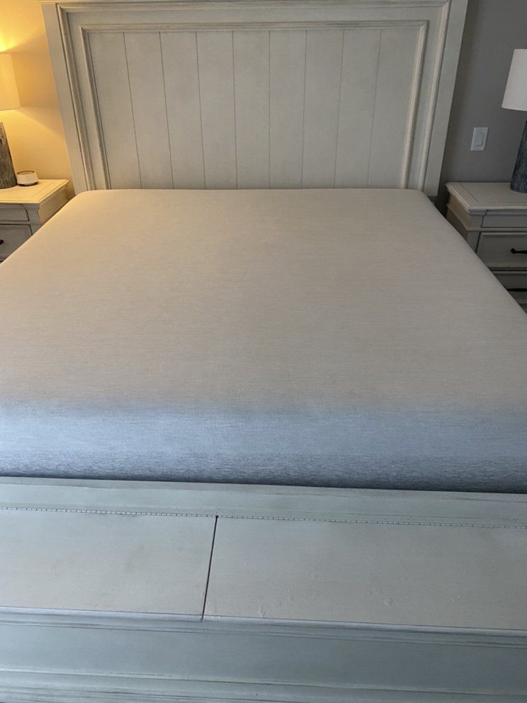 A bed with a white headboard and a white mattress in a bedroom.