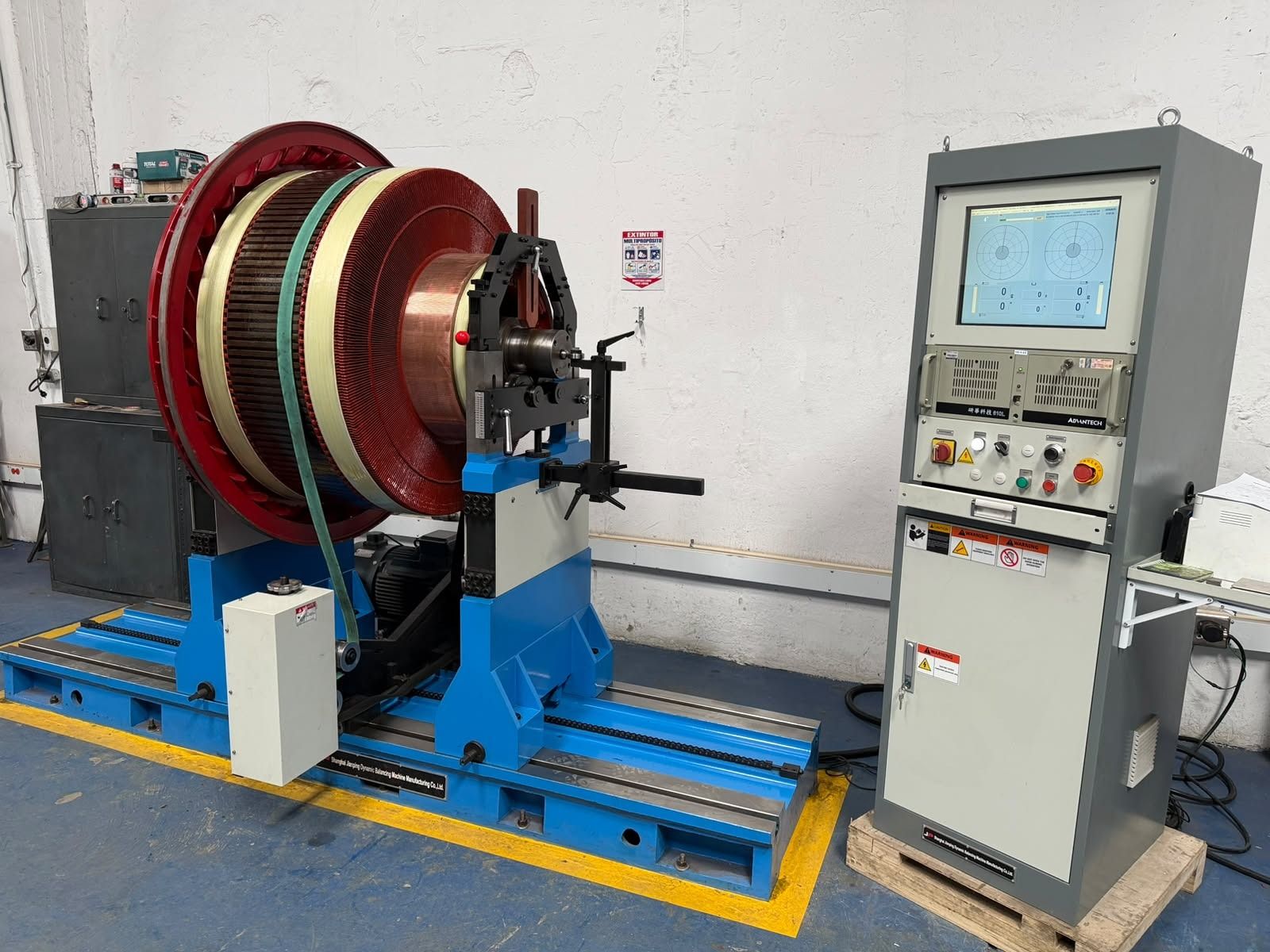 Máquina bobinadora de cables industrial con grandes carretes rojos y un armario de control en un taller.