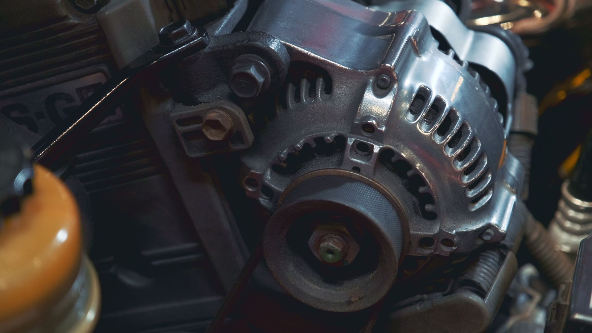 Primer plano de un alternador de motor de automóvil y sus componentes circundantes, con piezas metálicas y cables.