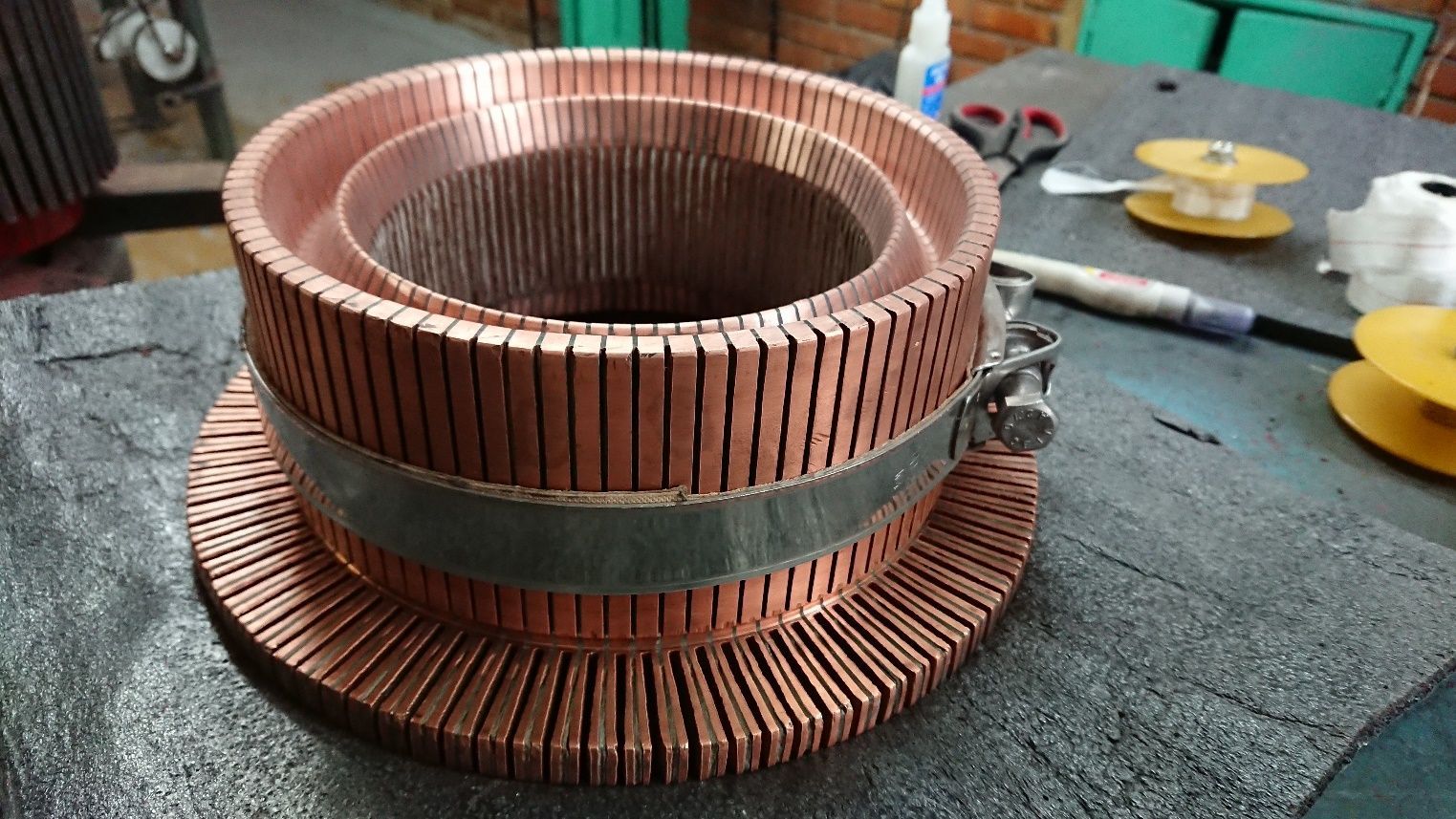 Bobina del estator de un motor eléctrico de color cobre sobre un banco de trabajo, sujeta por una banda metálica.