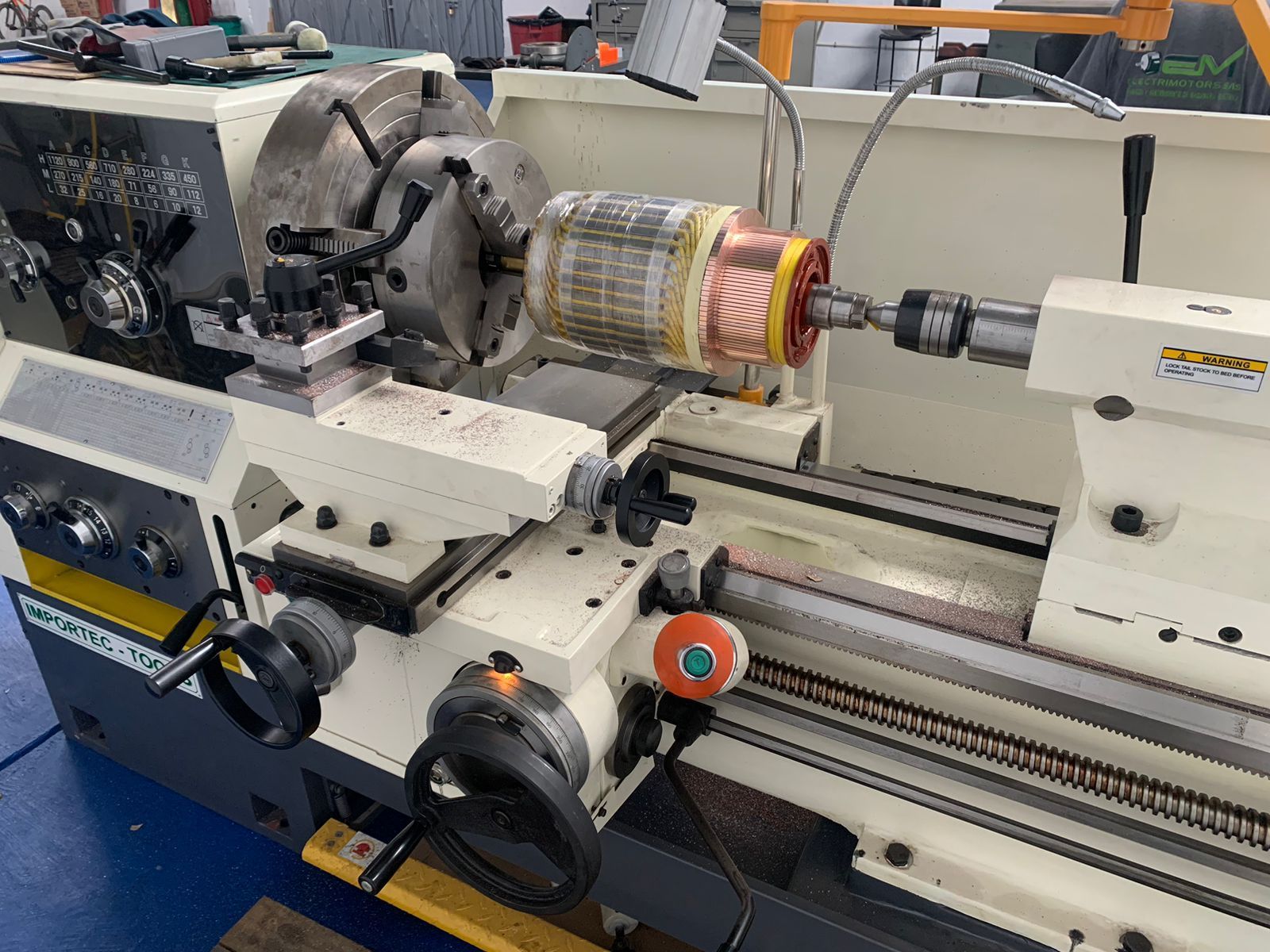 Torno industrial mecanizando una pieza cilíndrica en un taller, con virutas de metal y controles de la máquina visibles.