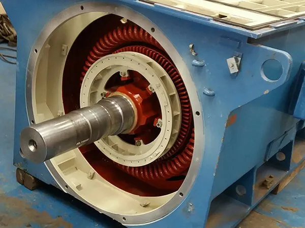 Primer plano de un motor eléctrico industrial azul con bobinados rojos expuestos y un eje metálico.