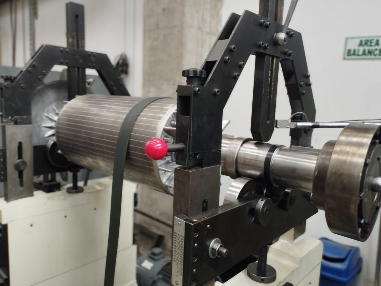 Máquina industrial con conjunto de rotor metálico sujeto en un banco de equilibrado, con un marcador rojo colocado.