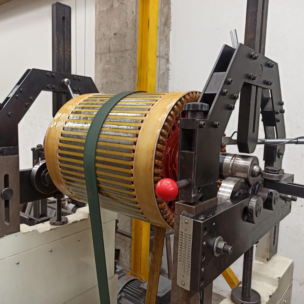 Máquina industrial con un rotor cilíndrico amarillo montado en un bastidor y correas de metal negro.