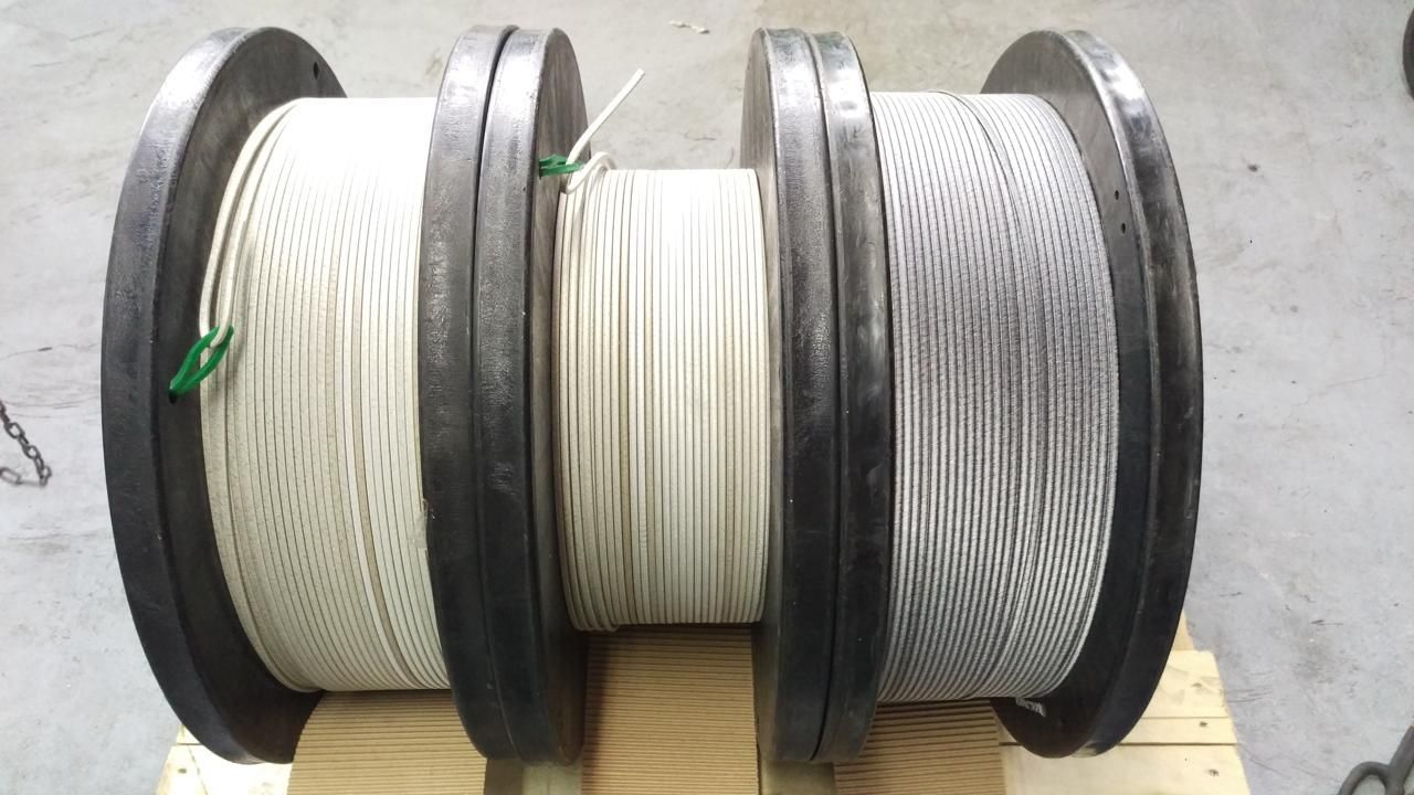 Tres grandes bobinas de alambre o cable sobre un palé de madera, con bobinas blancas y grises enrolladas en carretes negros.