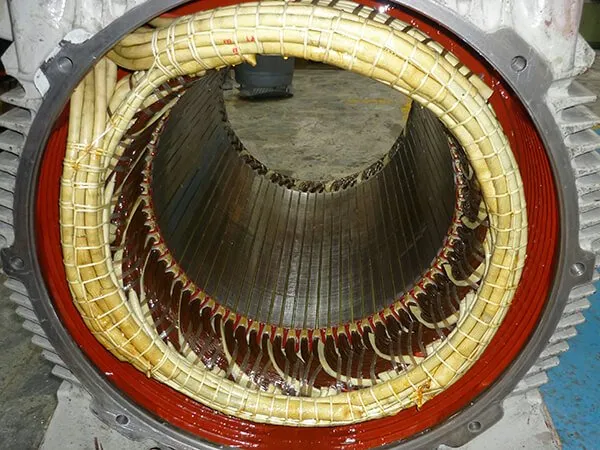 Primer plano del estator de un motor eléctrico con bobinados de cobre y un anillo interior rojo.