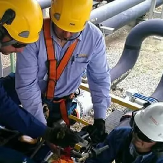 Tres trabajadores con cascos inspeccionan la maquinaria en una plataforma industrial.